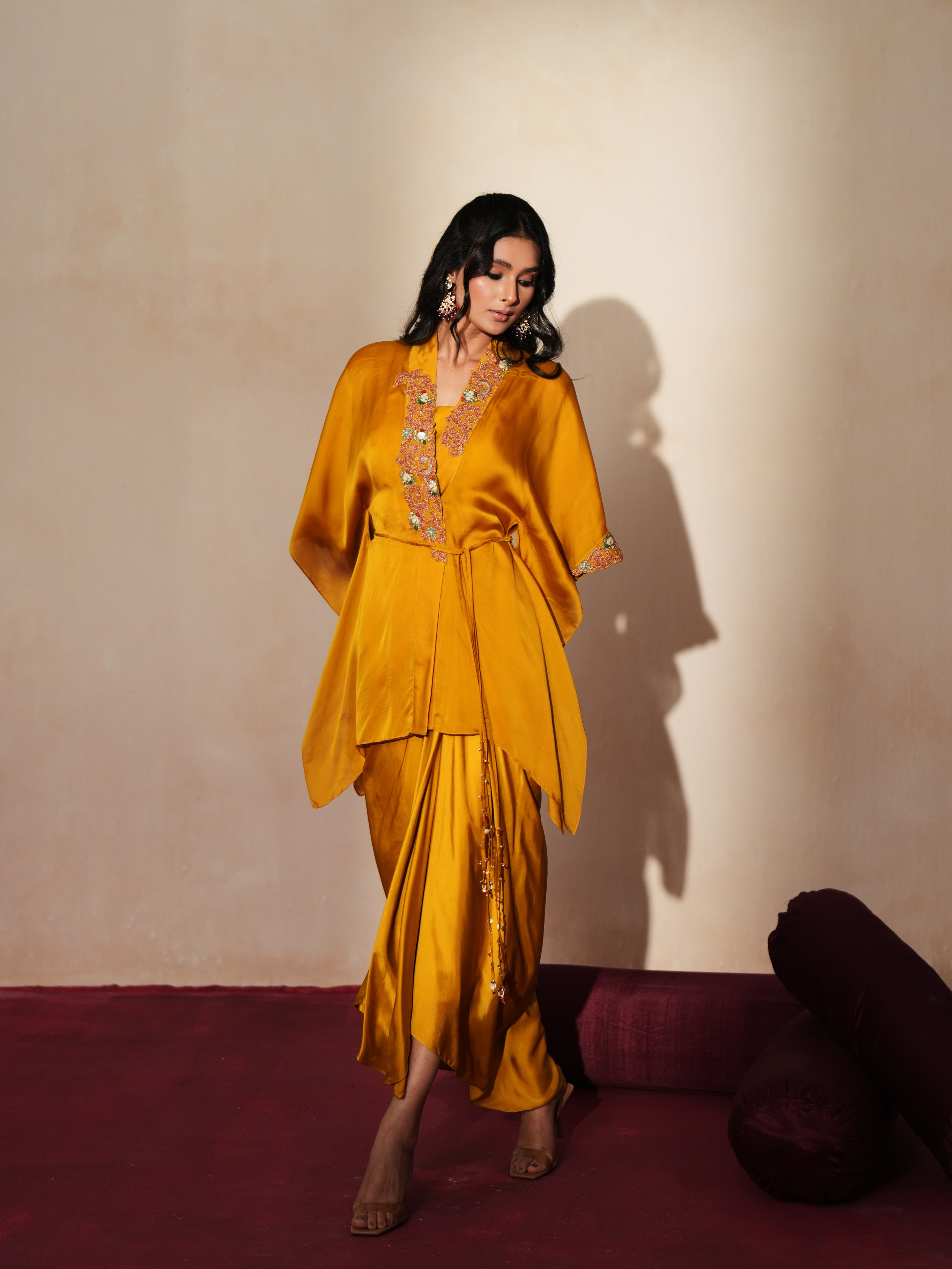 Woman in a golden yellow traditional outfit standing againsta beige wall on a red carpet.