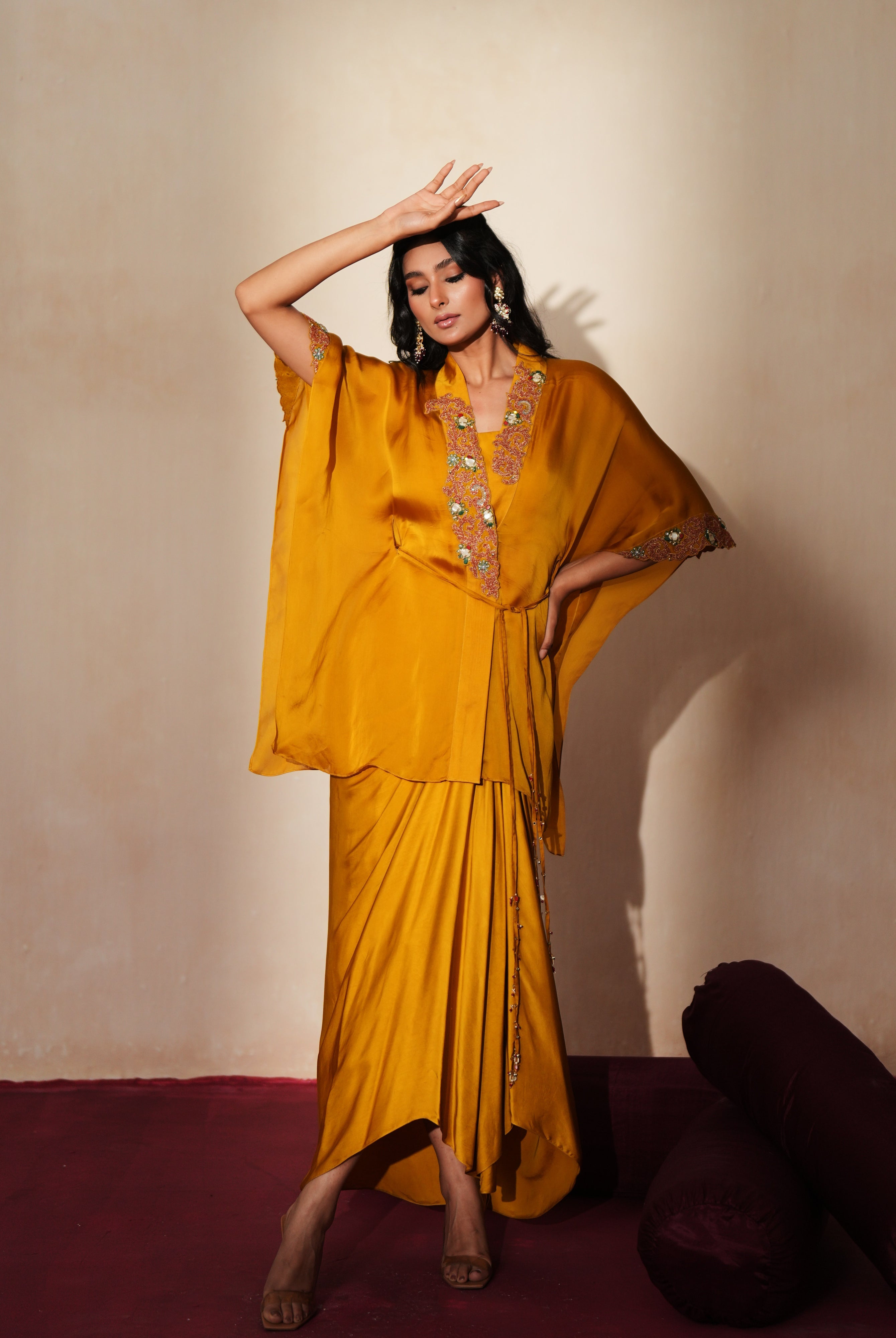 Woman in a golden yellow traditional outfit standing againsta beige wall on a red carpet.