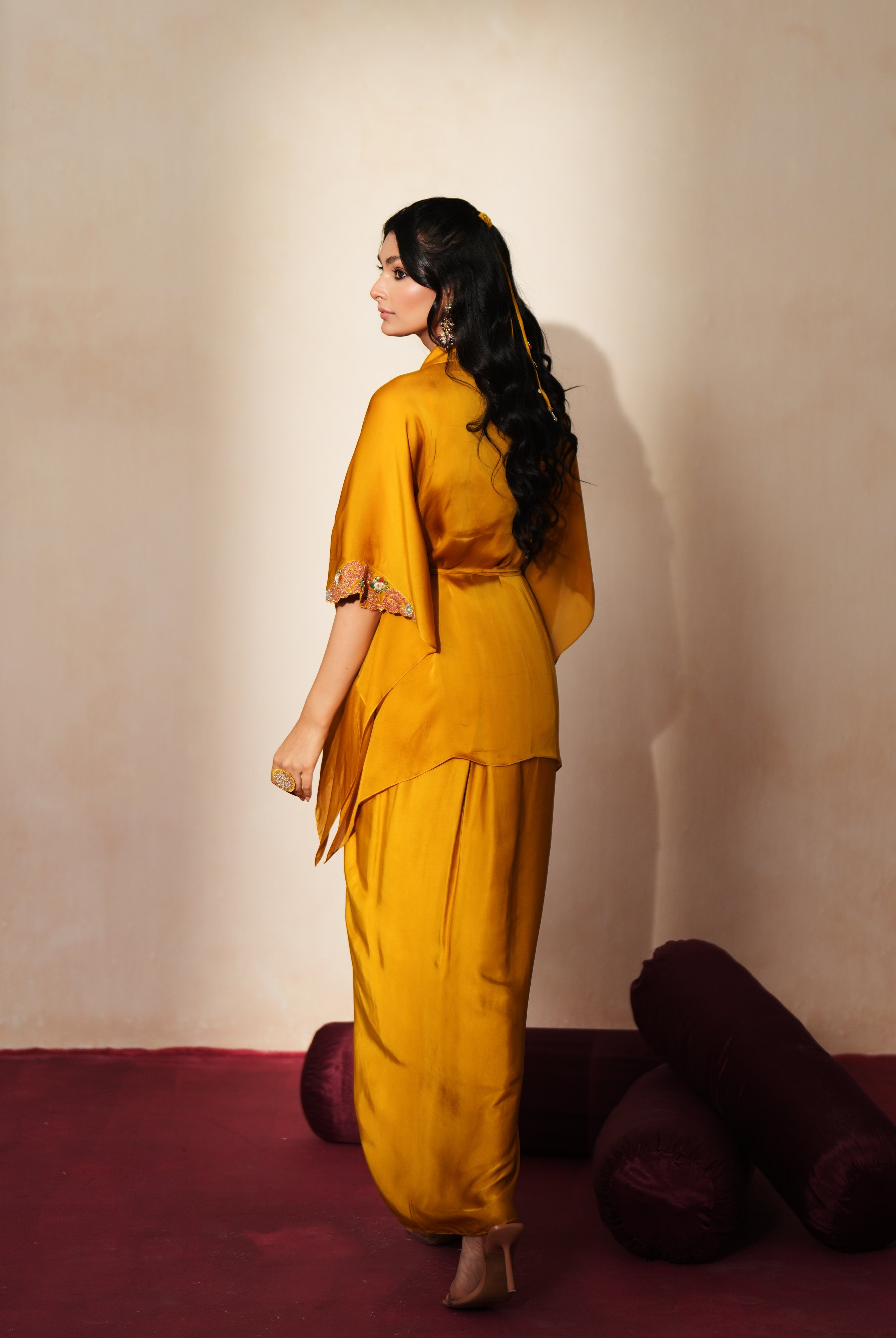 Woman in a golden yellow traditional outfit standing againsta beige wall on a red carpet.