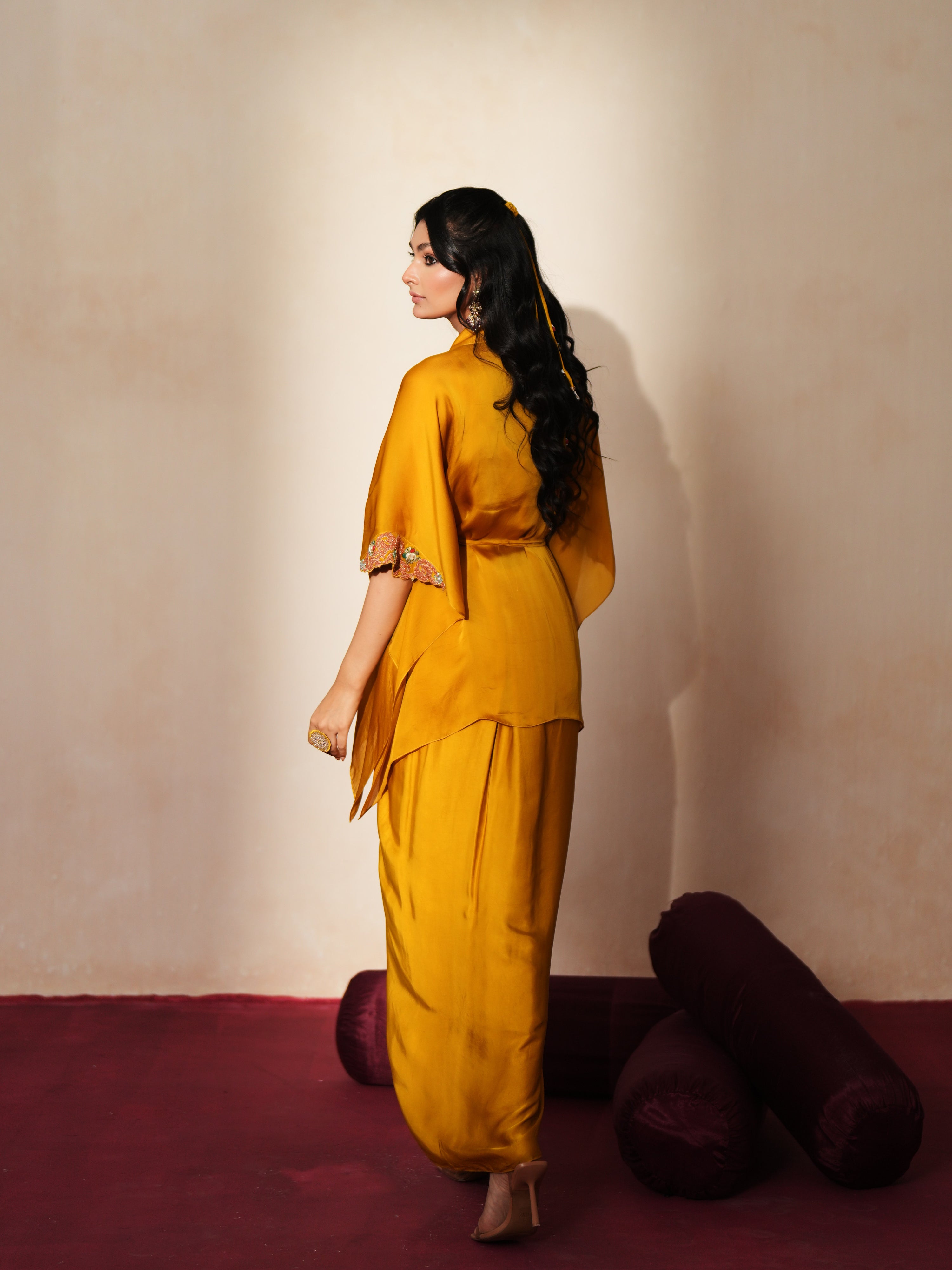 Woman in a golden yellow traditional outfit standing againsta beige wall on a red carpet.