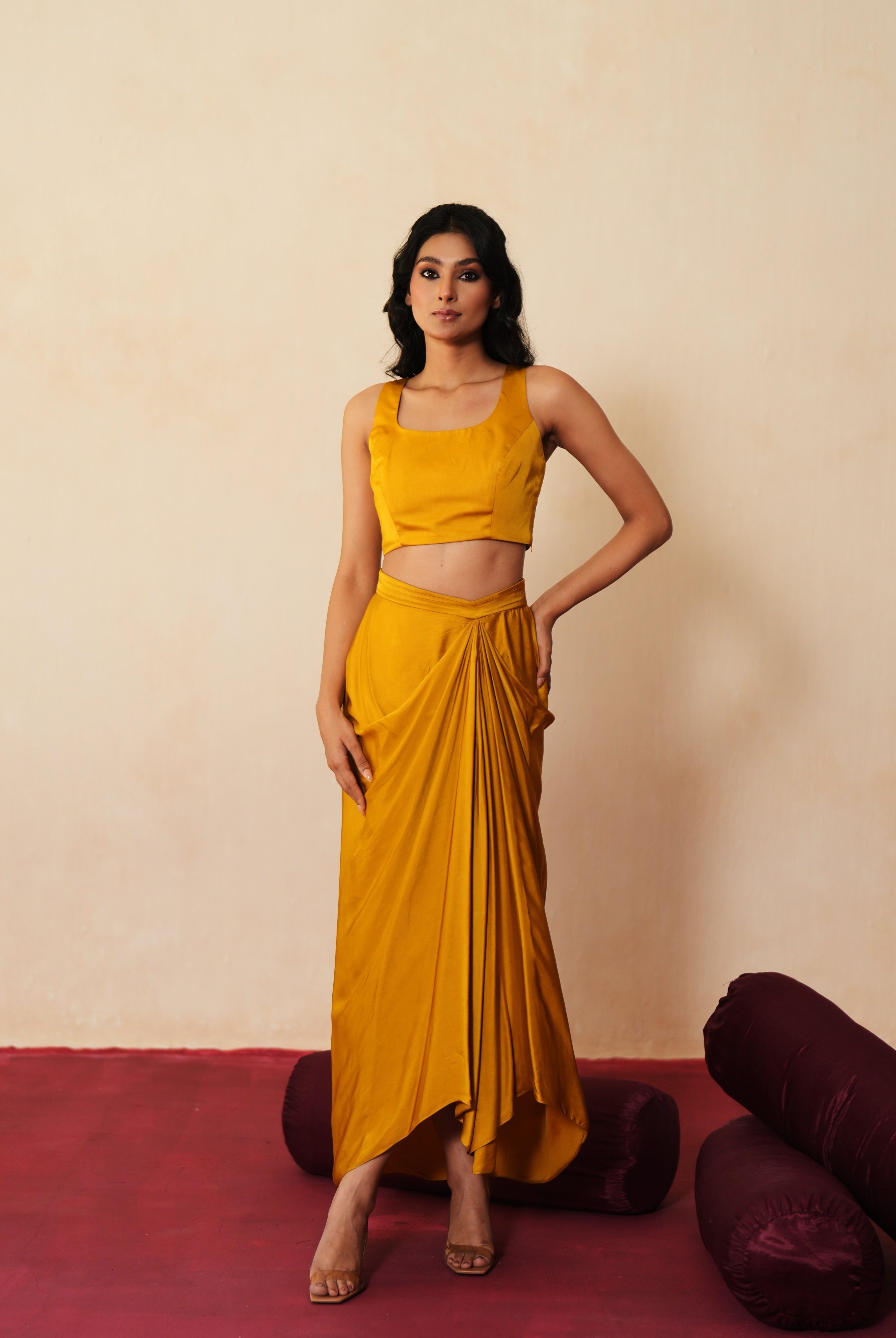 Woman in a golden yellow traditional outfit standing againsta beige wall on a red carpet.