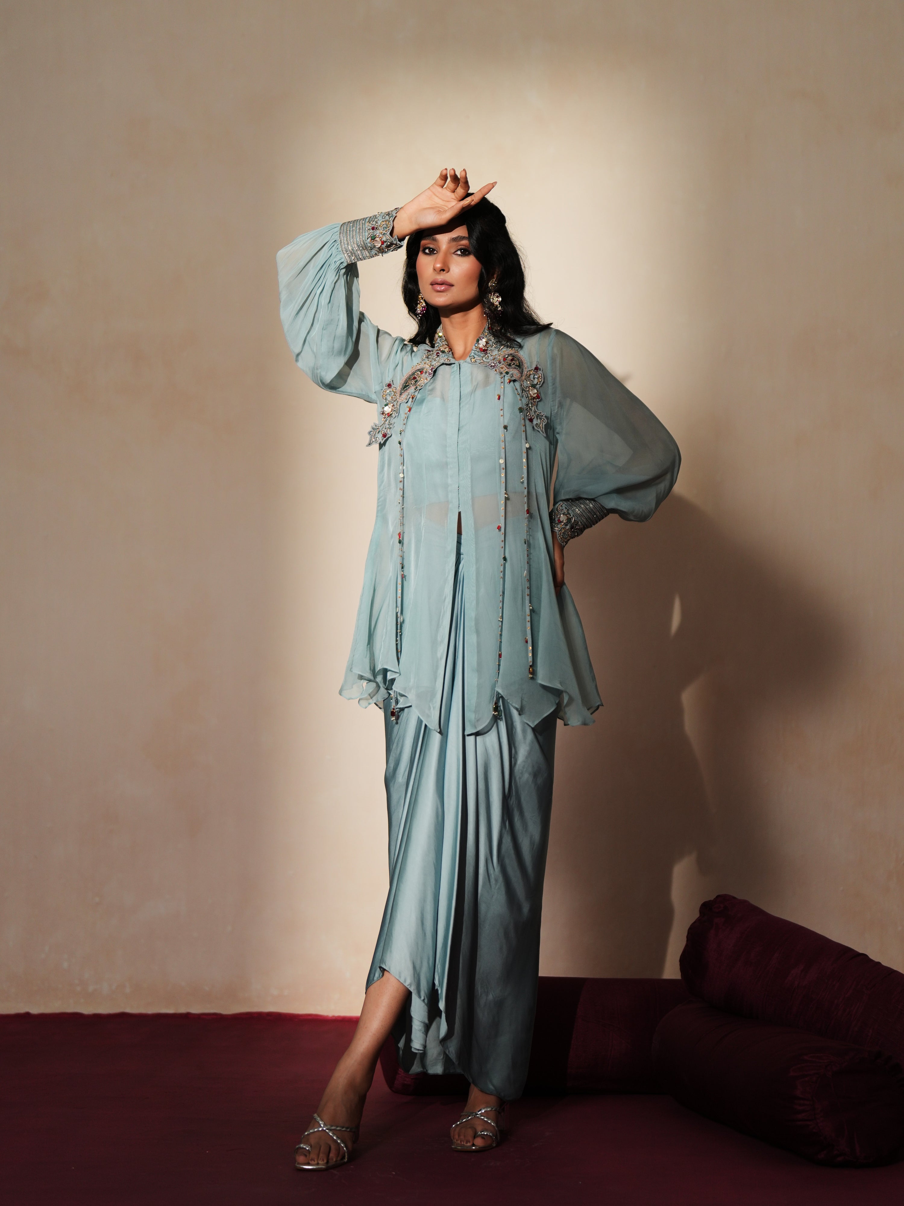 Woman in a pastel blue traditional outfit standing againsta beige wall on a red carpet.