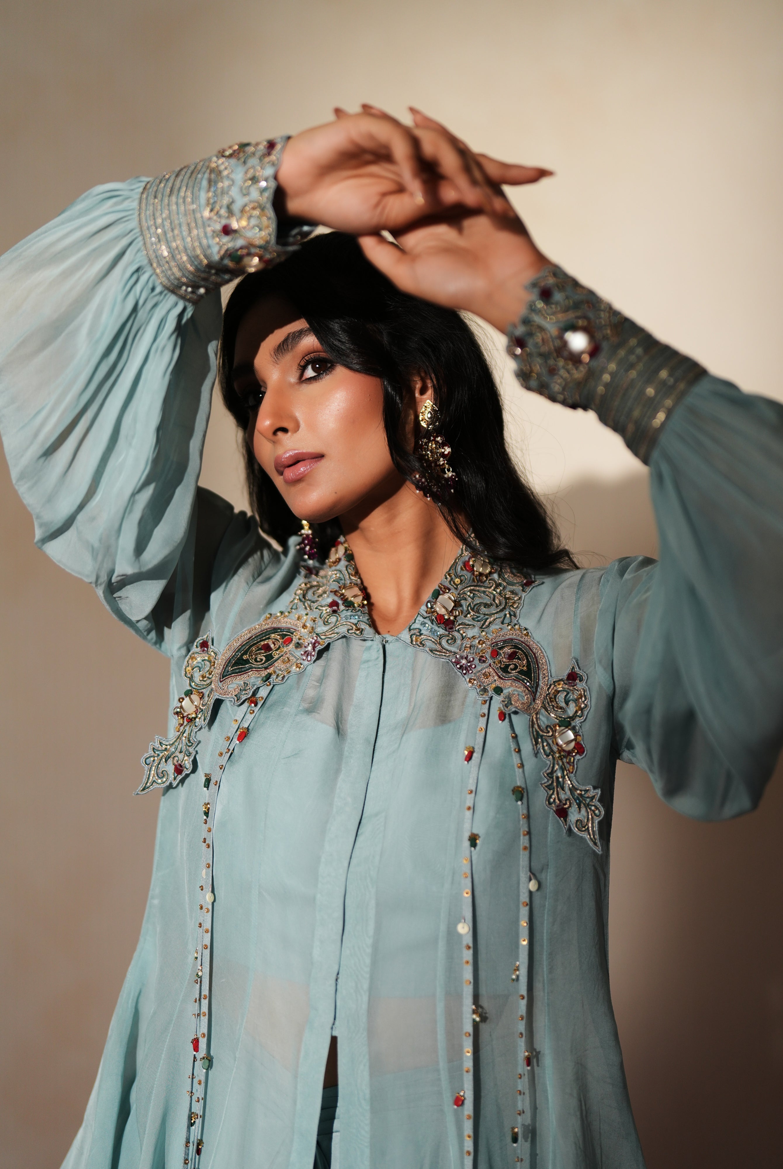 Woman in a pastel blue traditional outfit standing againsta beige wall on a red carpet.