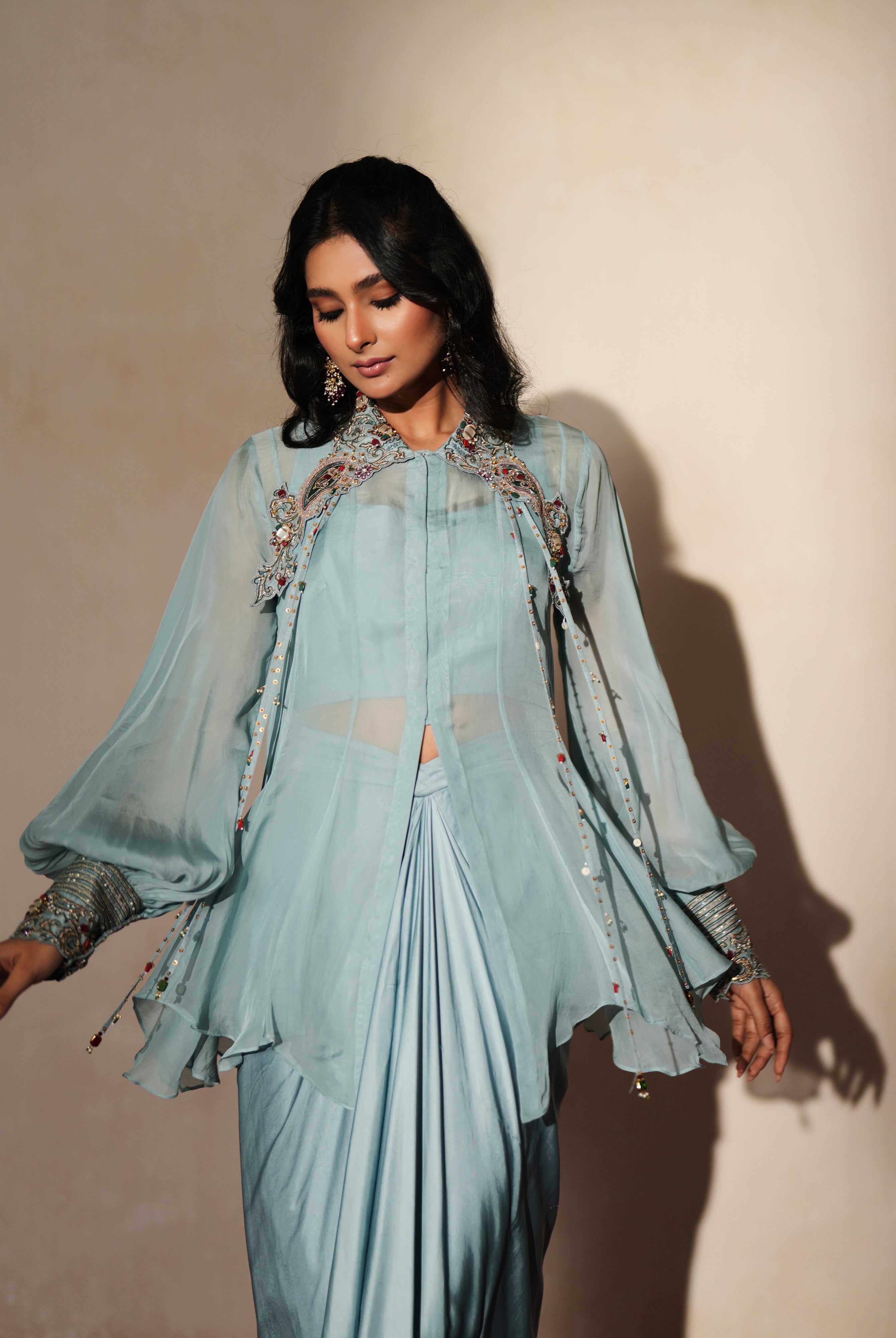 Woman in a pastel blue traditional outfit standing againsta beige wall on a red carpet.