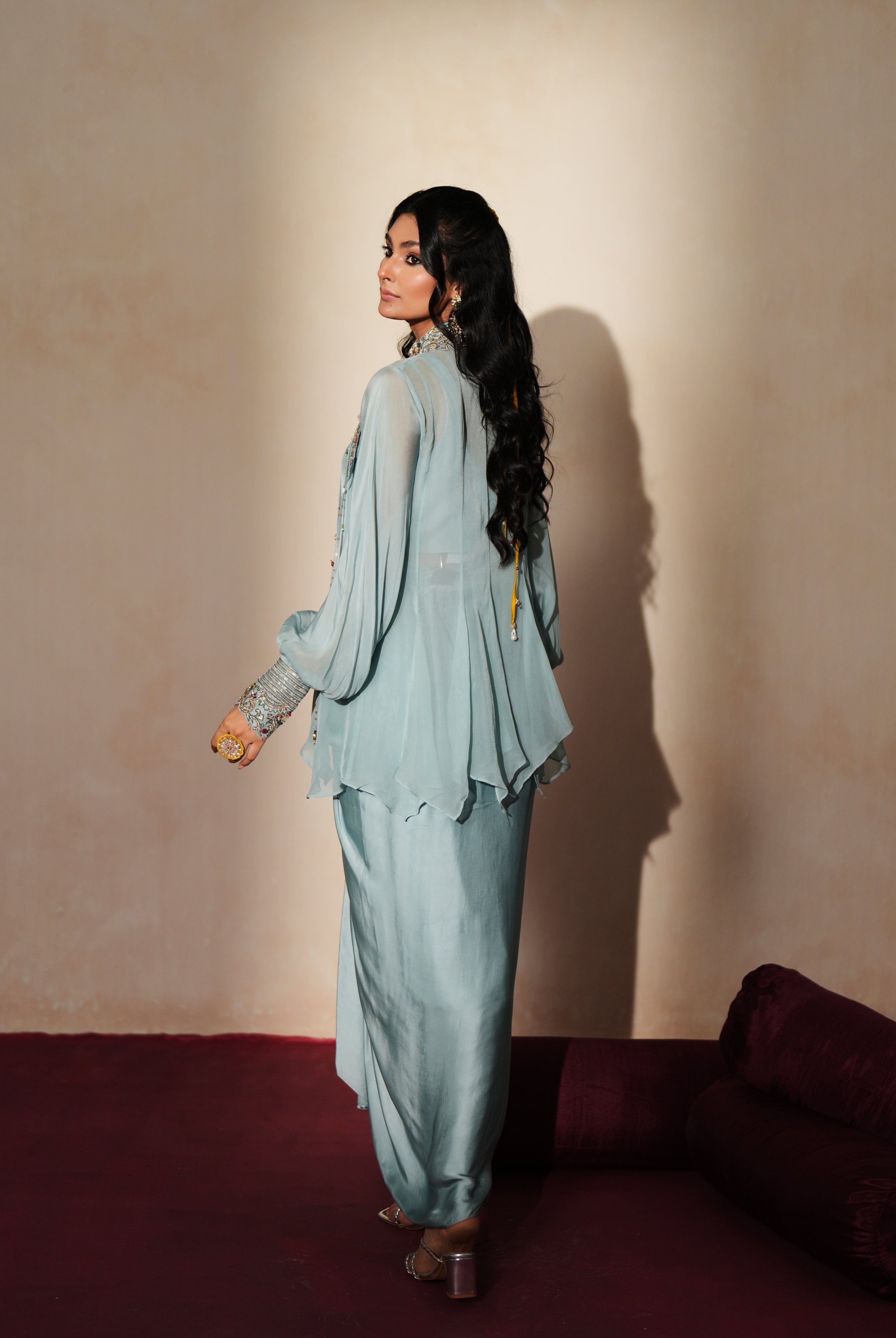 Woman in a pastel blue traditional outfit standing againsta beige wall on a red carpet.