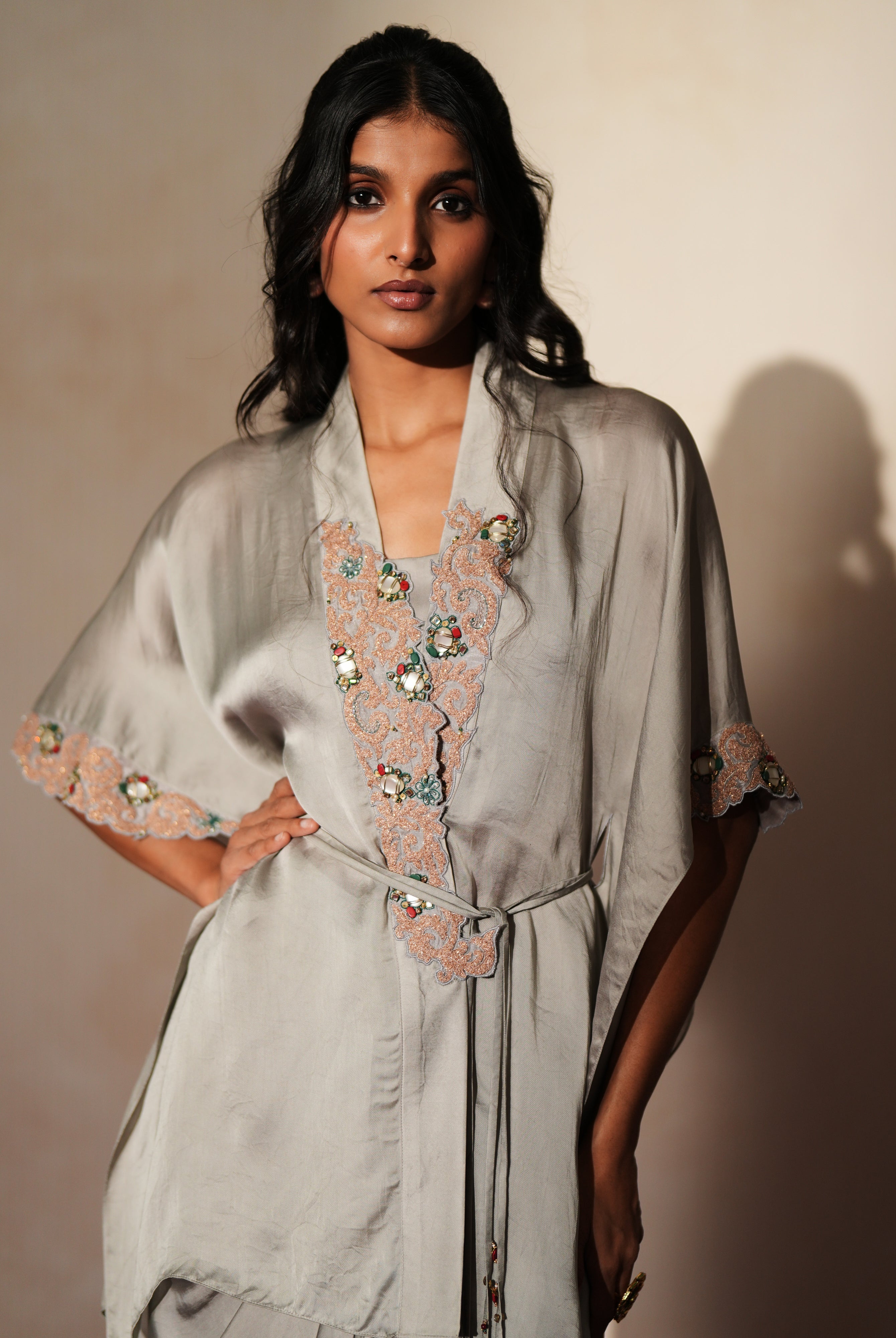 Woman in a mettalic grey traditional outfit standing againsta beige wall on a red carpet.