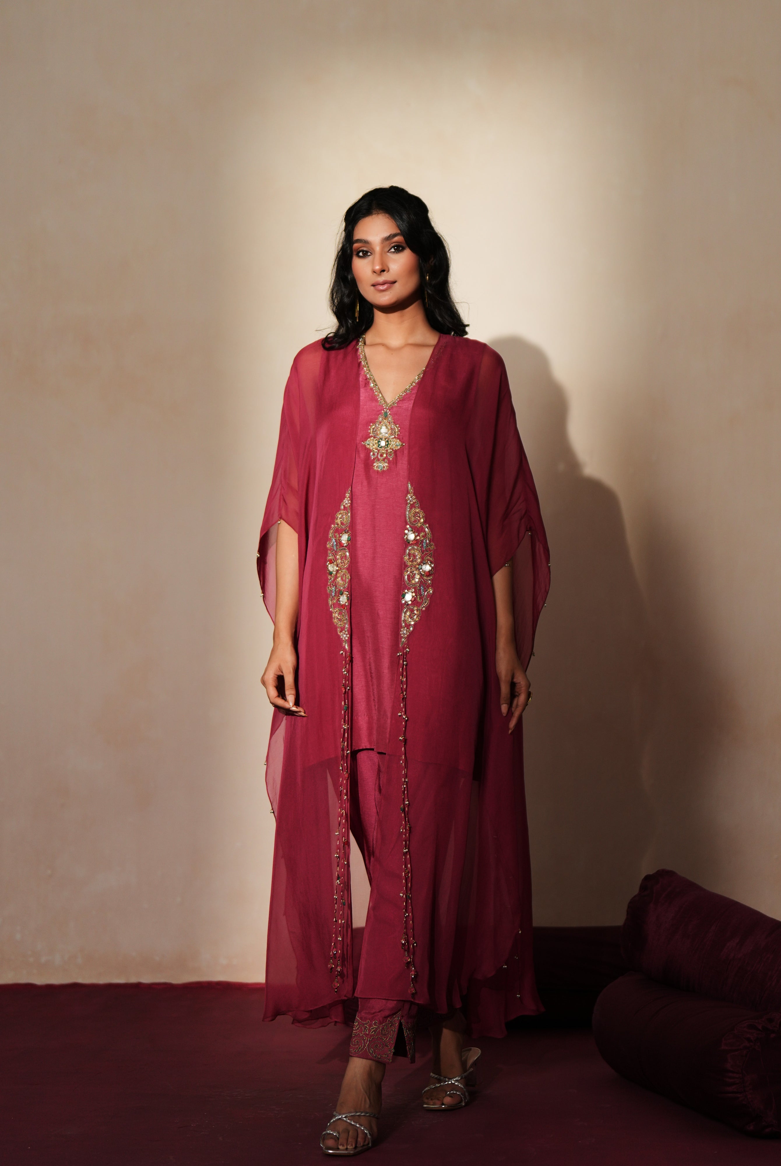 Woman in a mauve pink traditional outfit standing againsta beige wall on a red carpet.