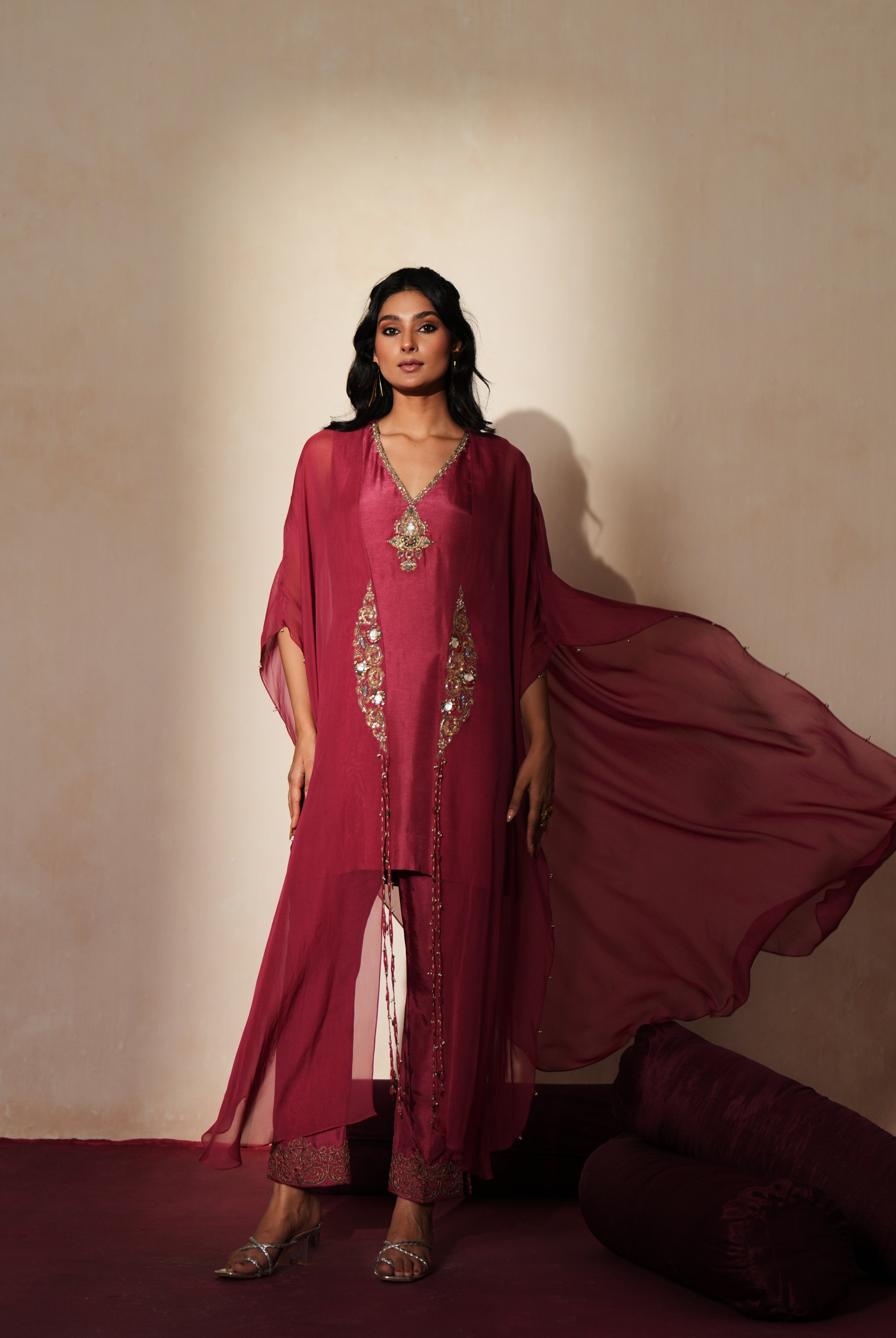 Woman in a mauve pink traditional outfit standing againsta beige wall on a red carpet.