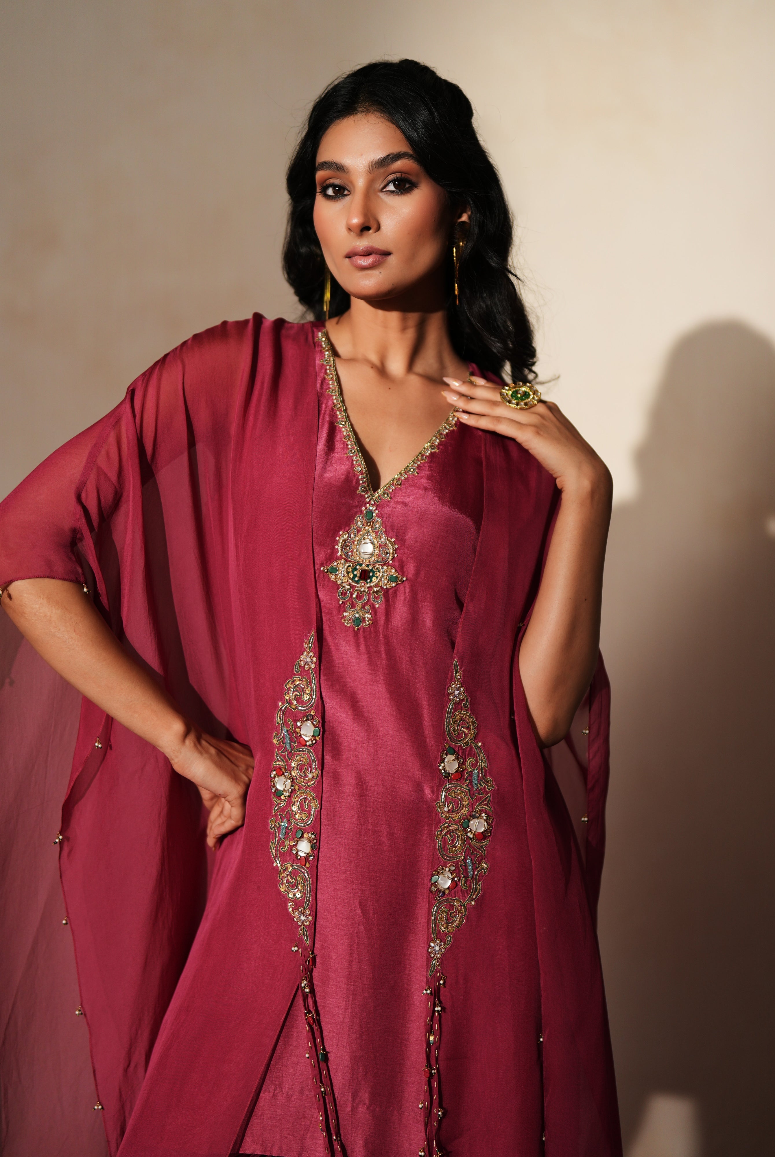 Woman in a mauve pink traditional outfit standing againsta beige wall on a red carpet.