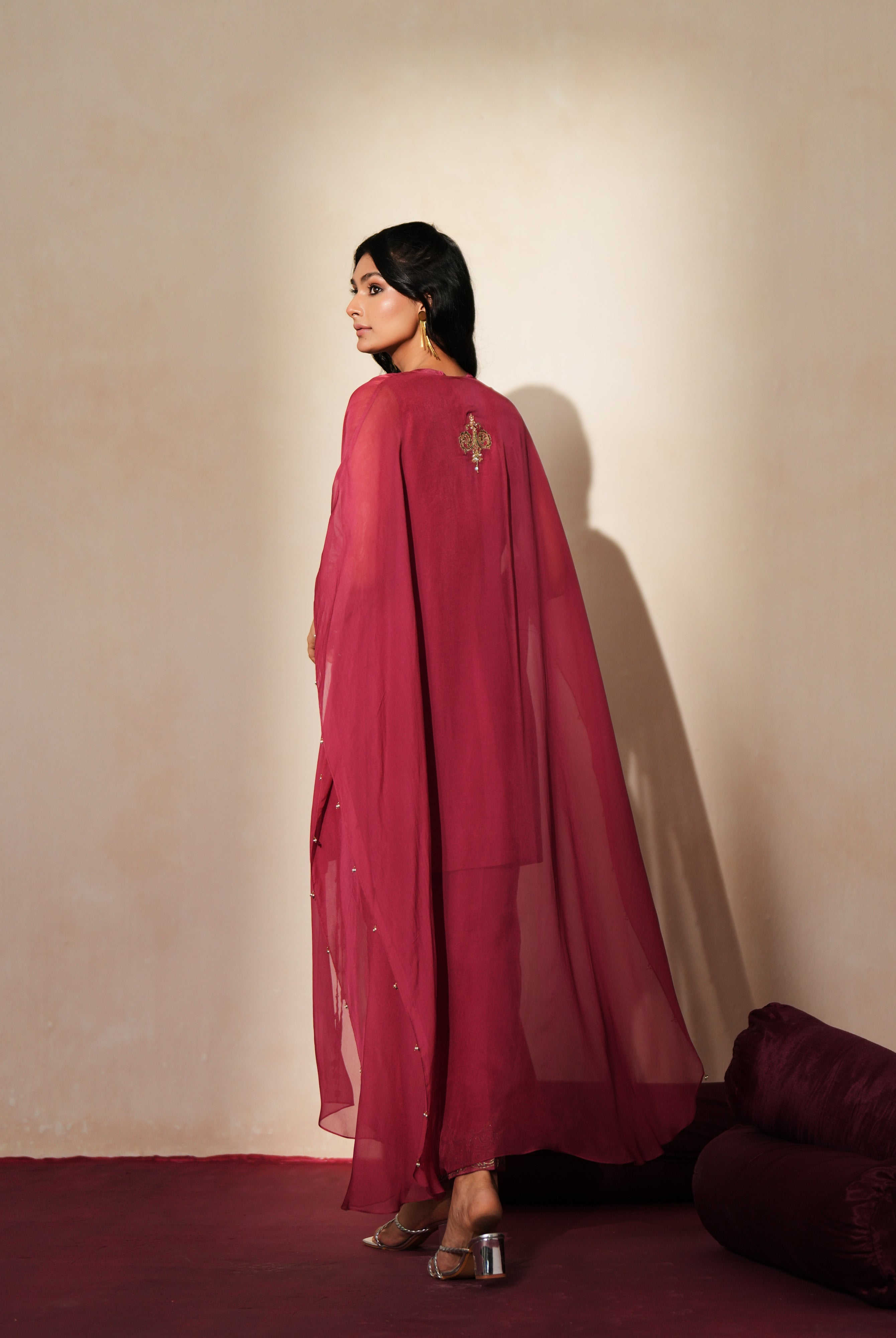 Woman in a mauve pink traditional outfit standing againsta beige wall on a red carpet.