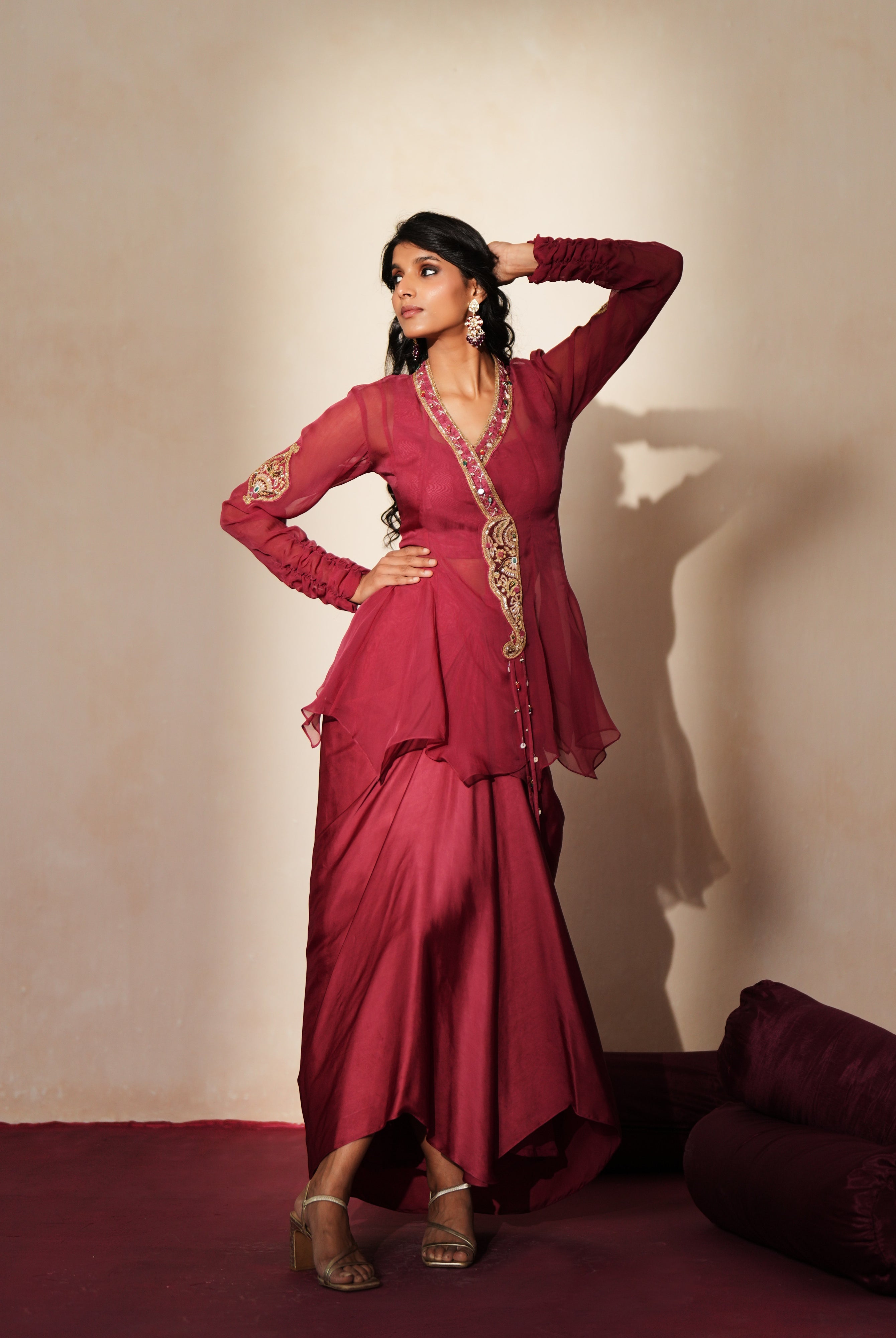 Woman in a mauve pink traditional outfit standing againsta beige wall on a red carpet.