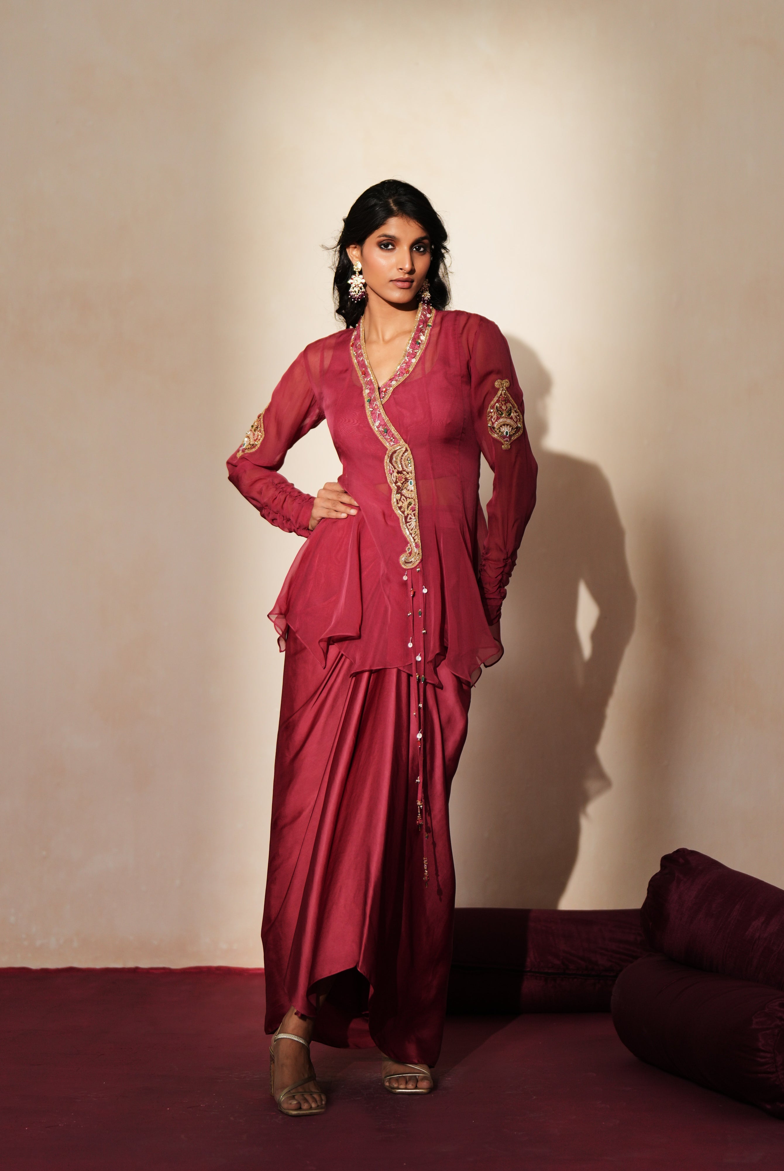 Woman in a mauve pink traditional outfit standing againsta beige wall on a red carpet.