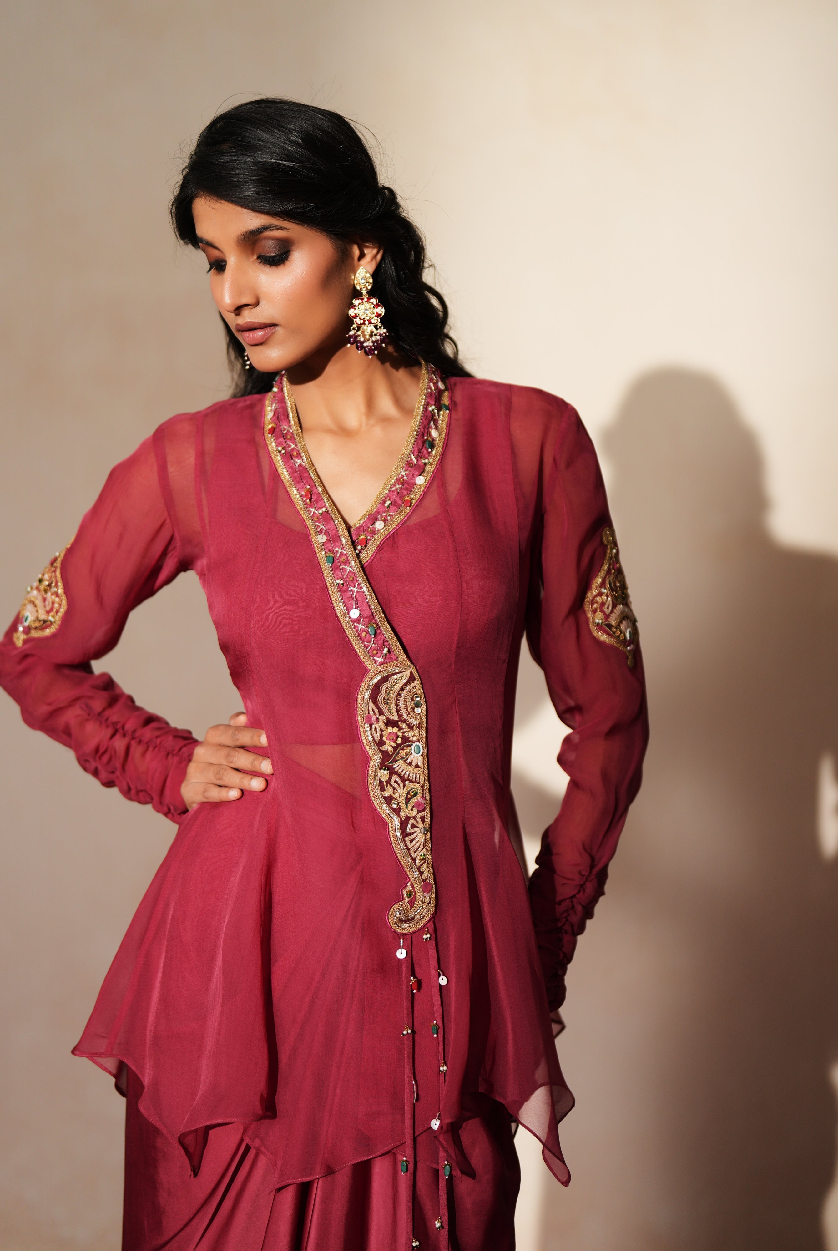 Woman in a mauve pink traditional outfit standing againsta beige wall on a red carpet.