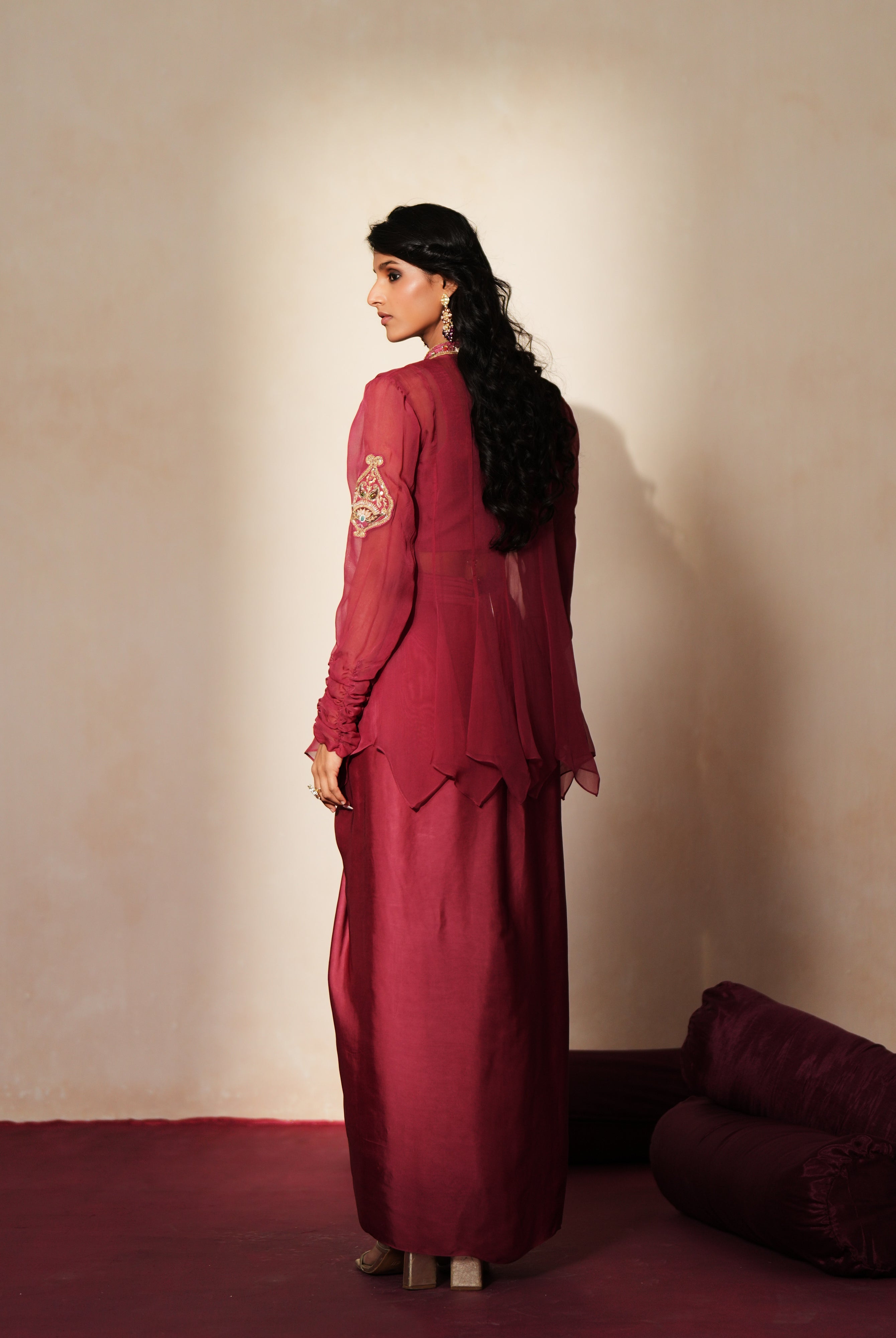 Woman in a mauve pink traditional outfit standing againsta beige wall on a red carpet.