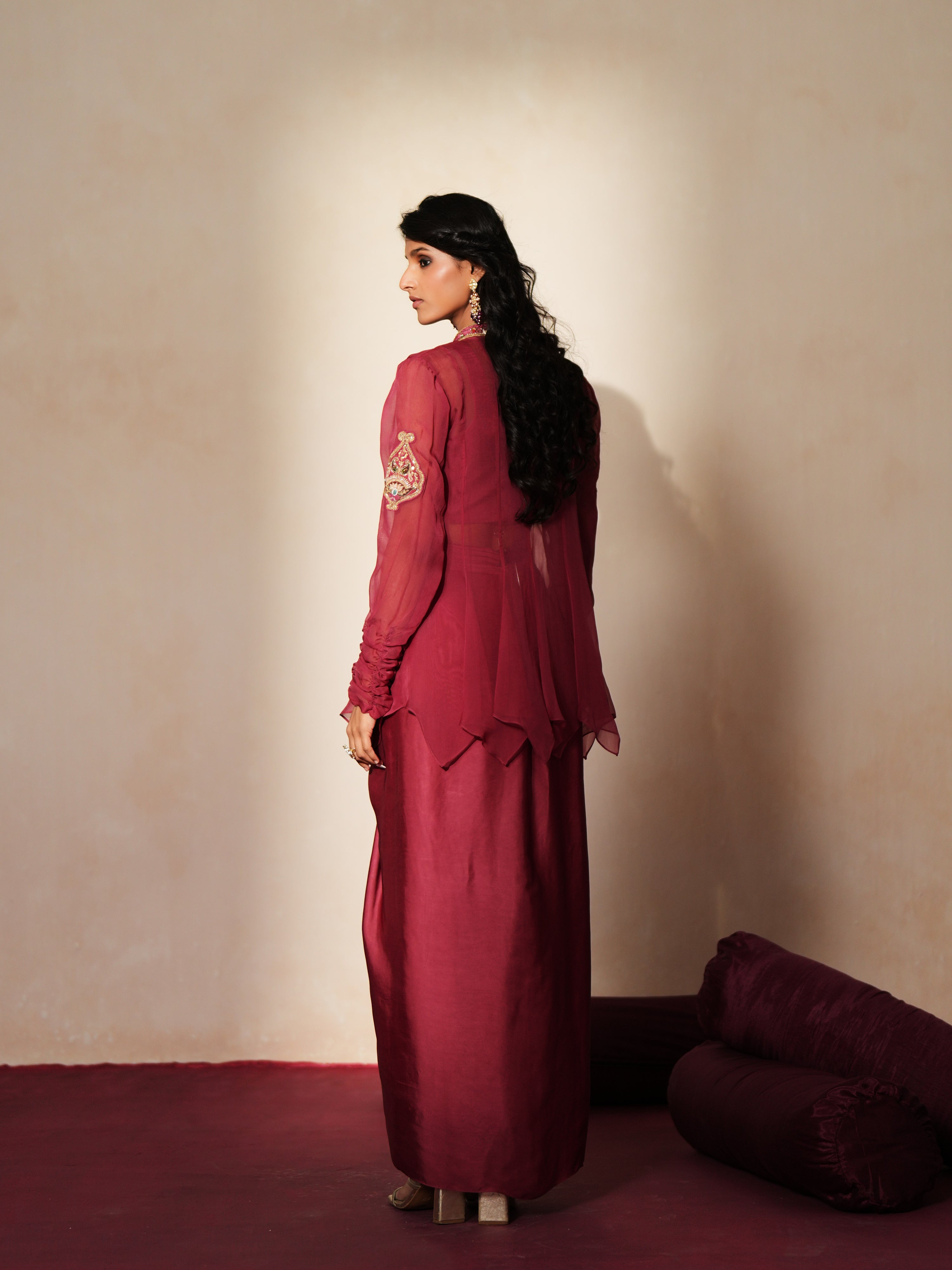Woman in a mauve pink traditional outfit standing againsta beige wall on a red carpet.