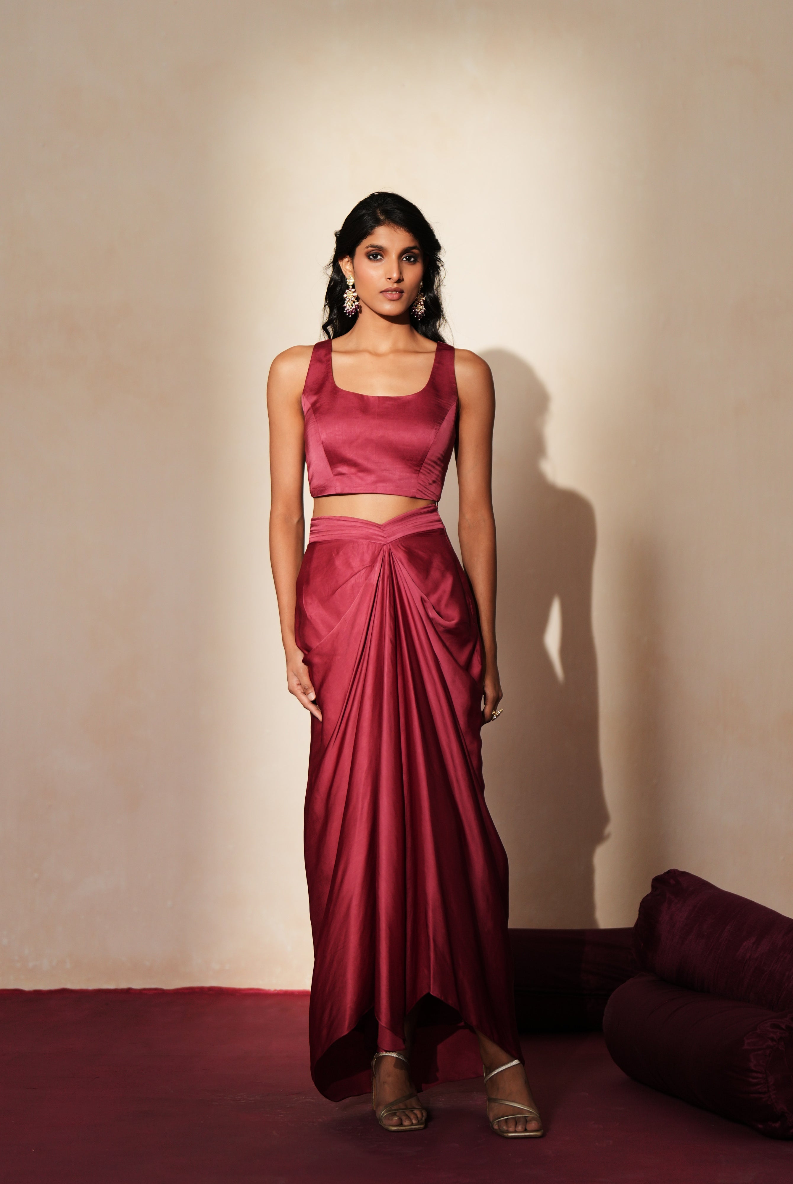 Woman in a mauve pink traditional outfit standing againsta beige wall on a red carpet.