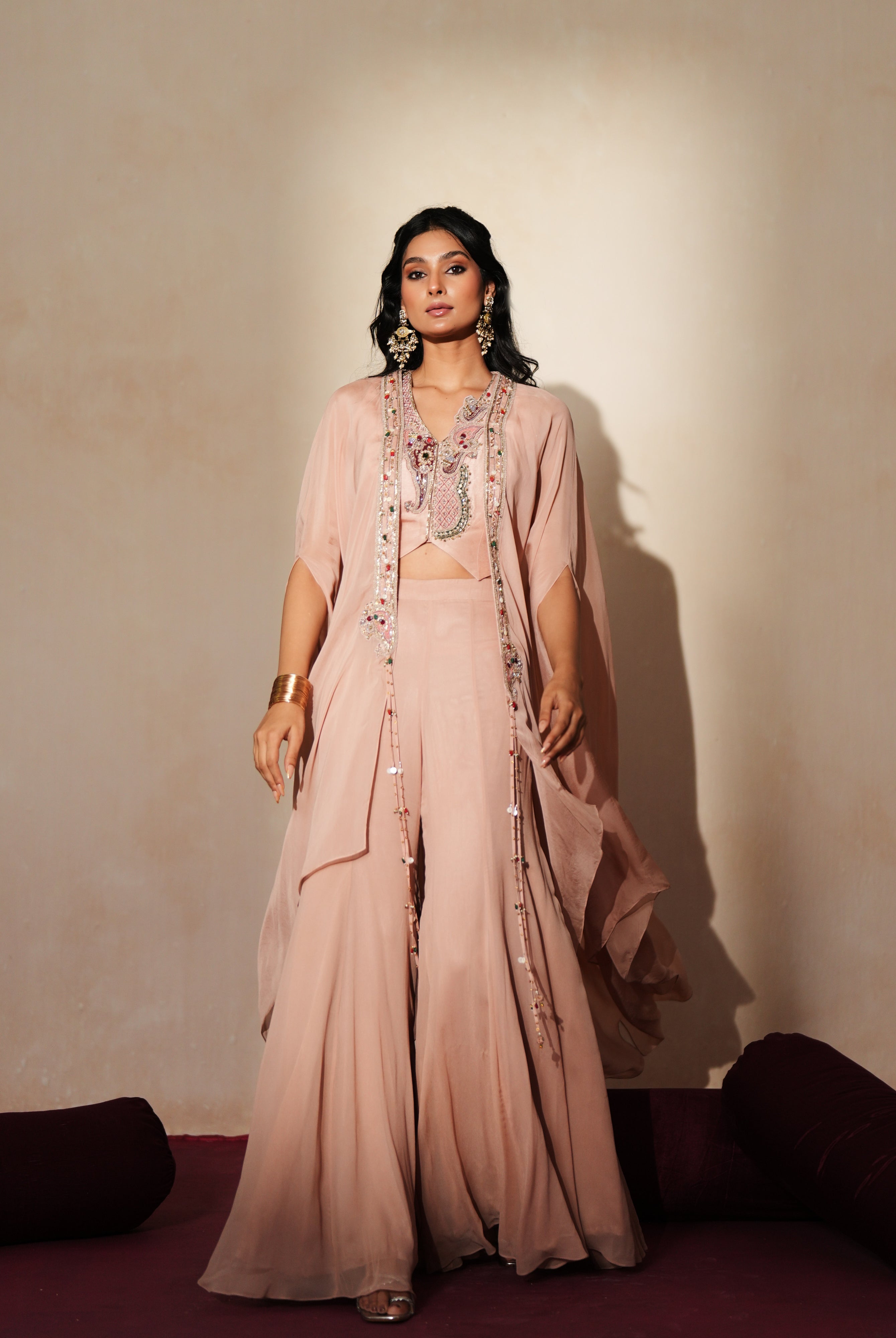 Woman in a soft pink traditional outfit standing againsta beige wall on a red carpet.