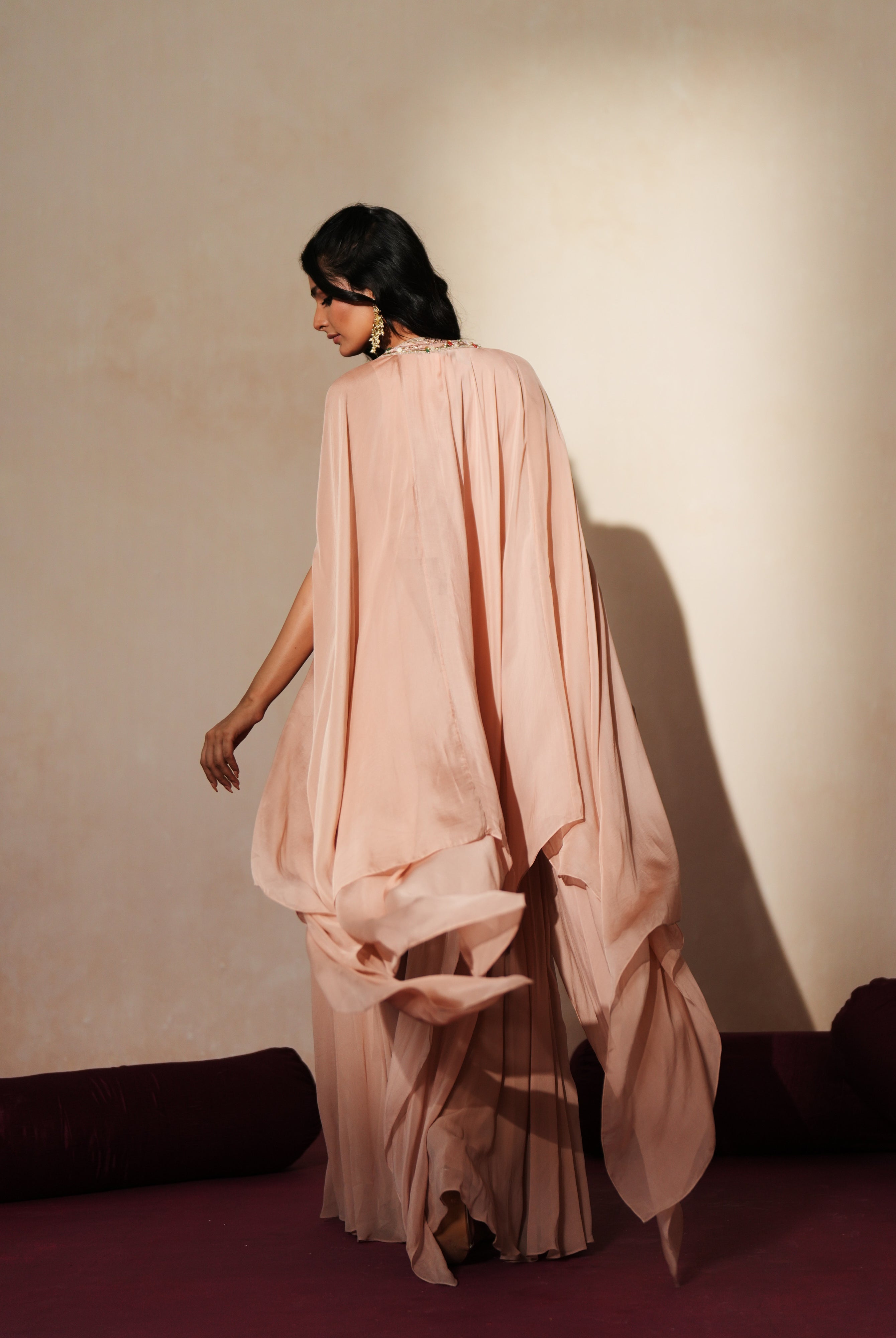 Woman in a soft pink traditional outfit standing againsta beige wall on a red carpet.