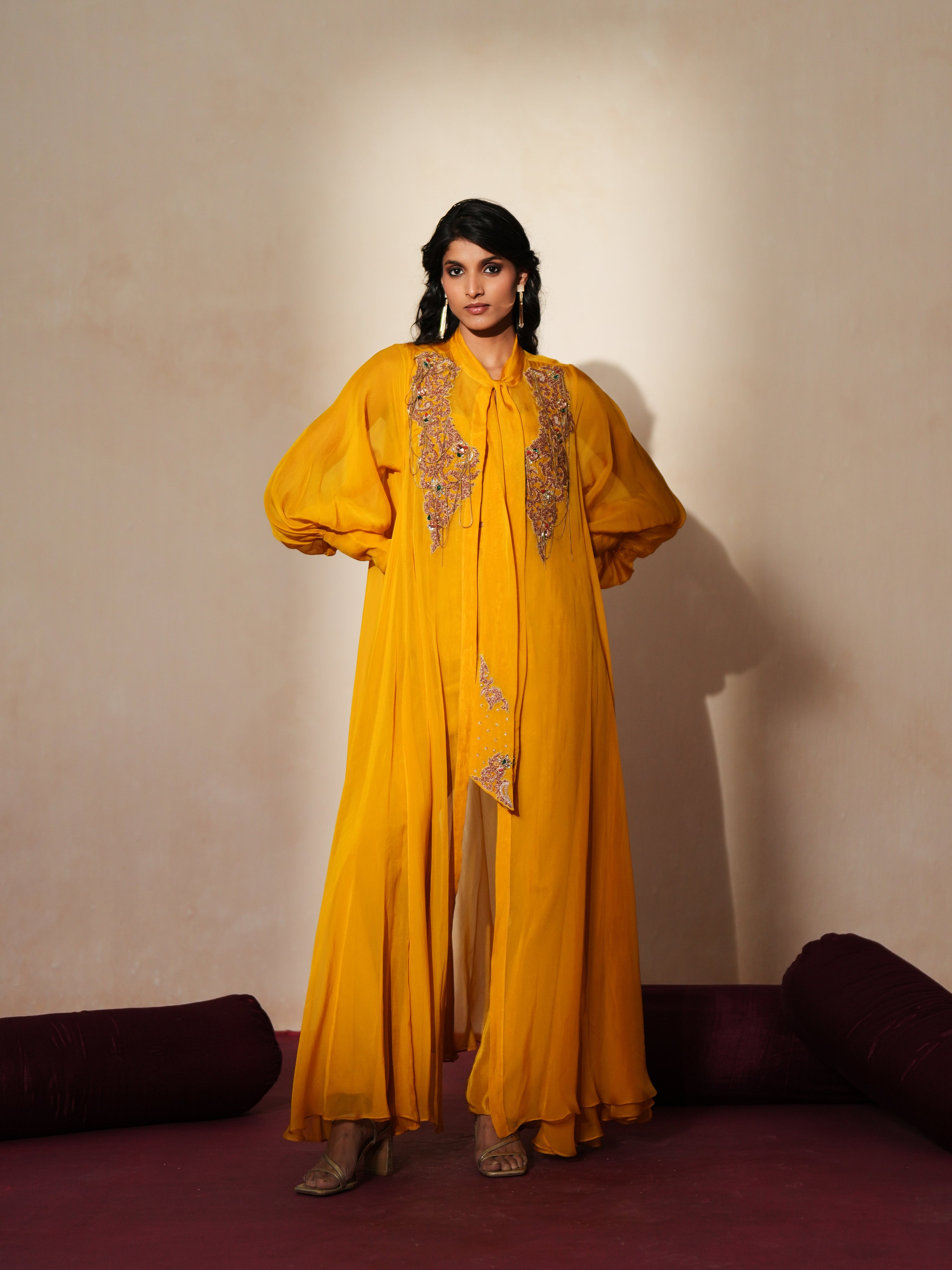 Woman in a golden yellow traditional outfit standing againsta beige wall on a red carpet.