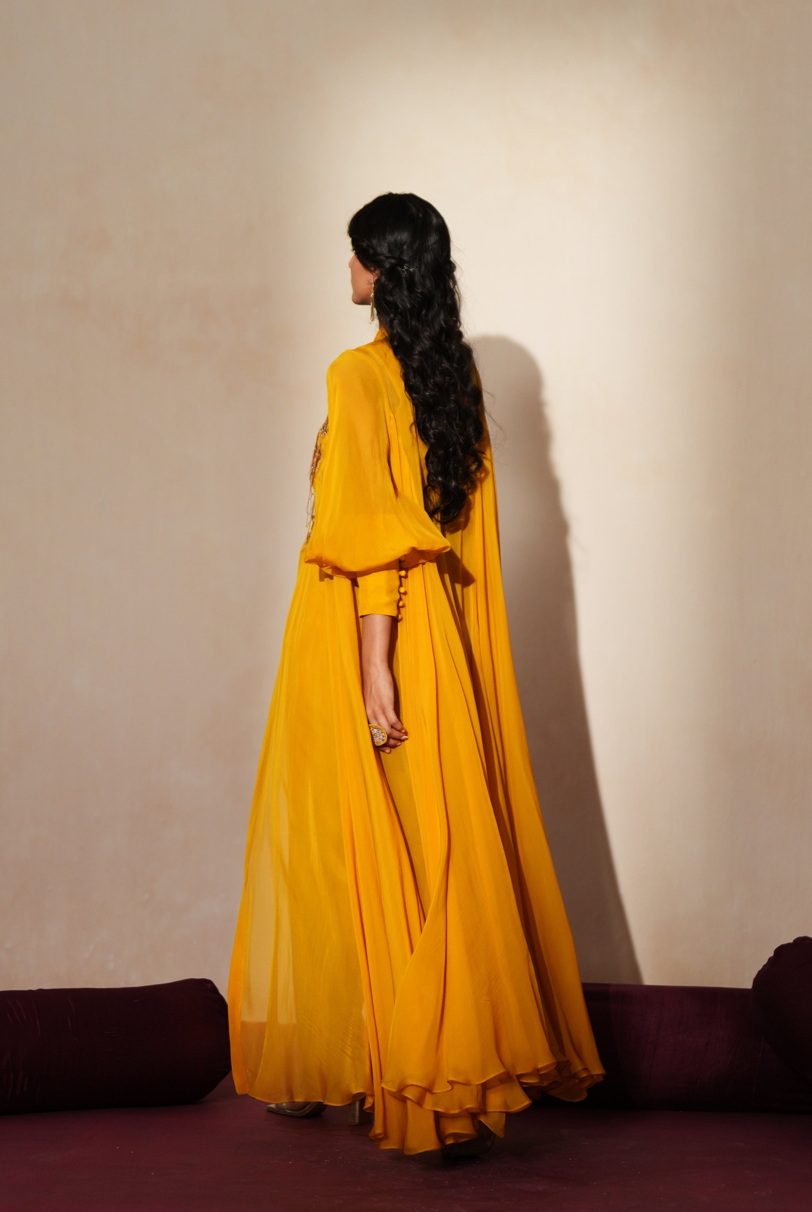 Woman in a golden yellow traditional outfit standing againsta beige wall on a red carpet.