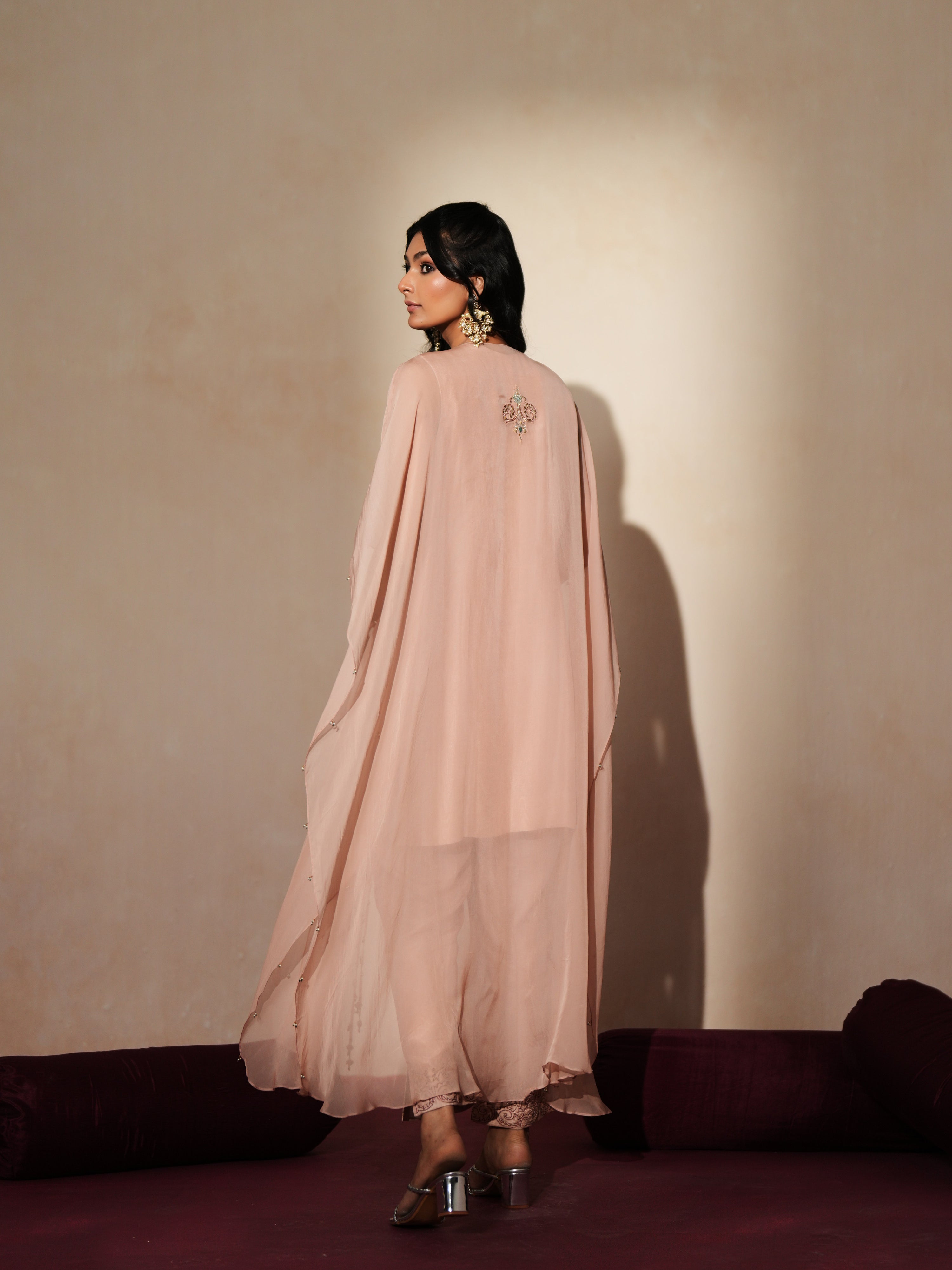 Woman in a soft pink traditional outfit standing againsta beige wall on a red carpet.