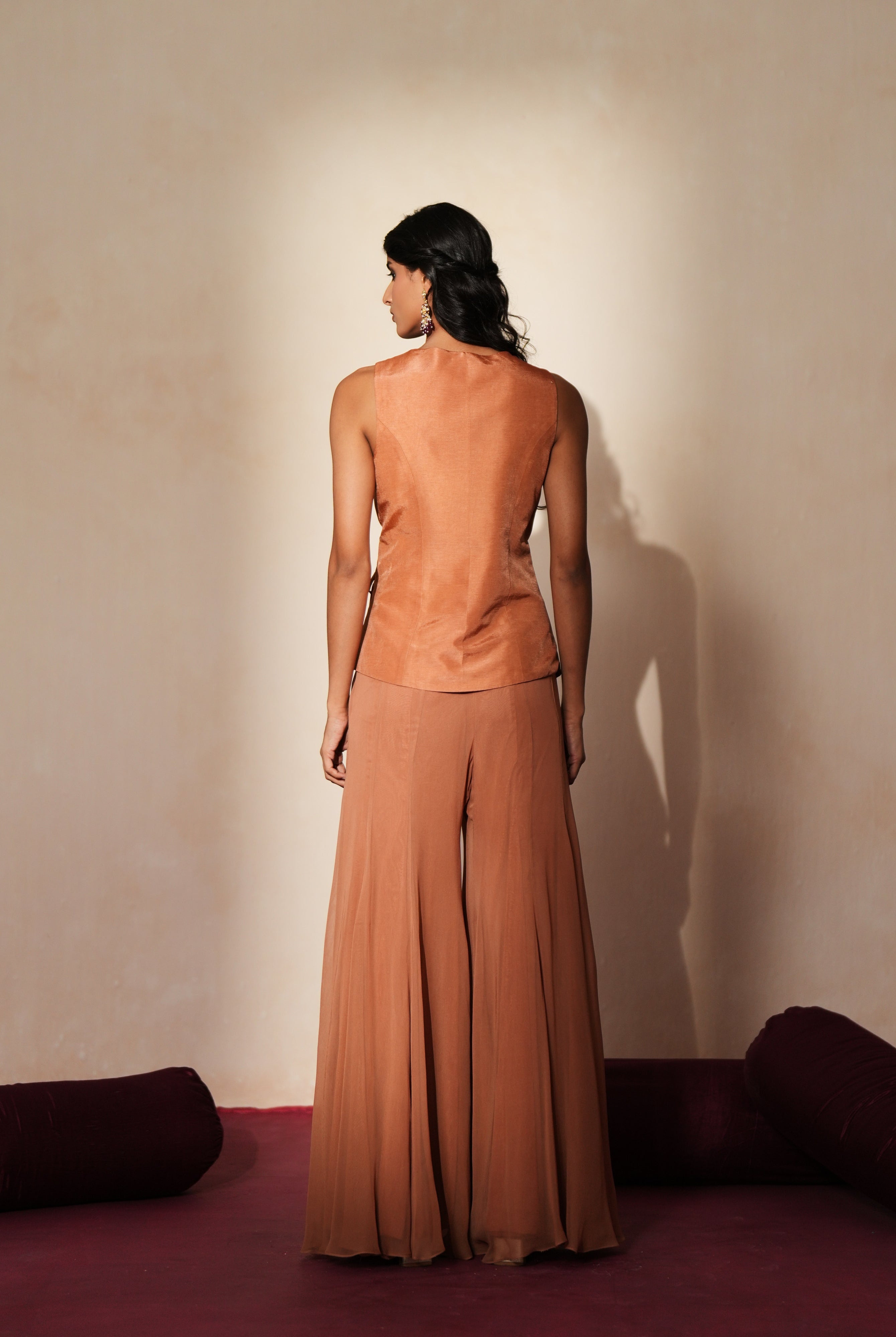 Woman in a metallic mocha traditional outfit standing againsta beige wall on a red carpet.