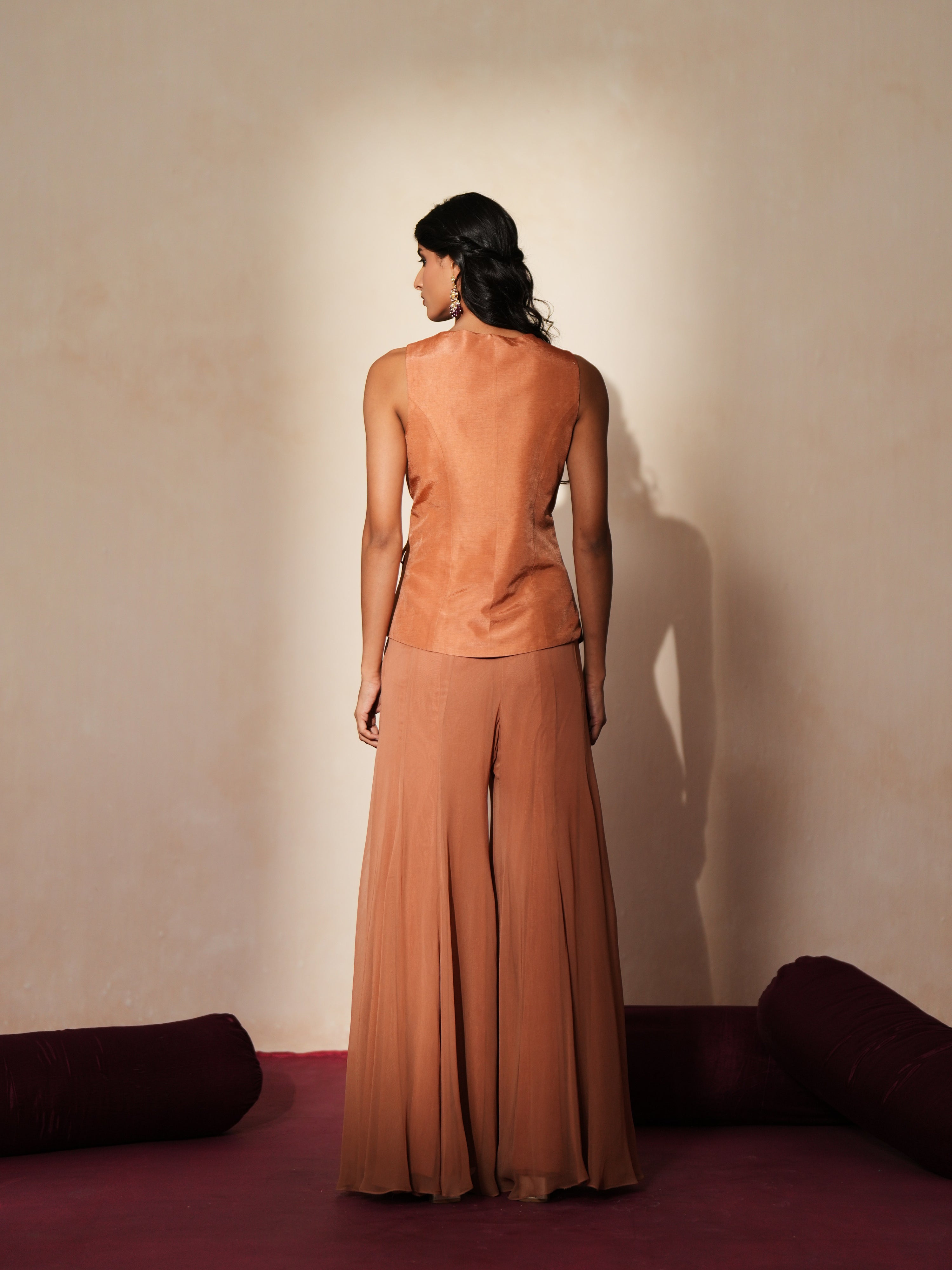 Woman in a metallic mocha traditional outfit standing againsta beige wall on a red carpet.