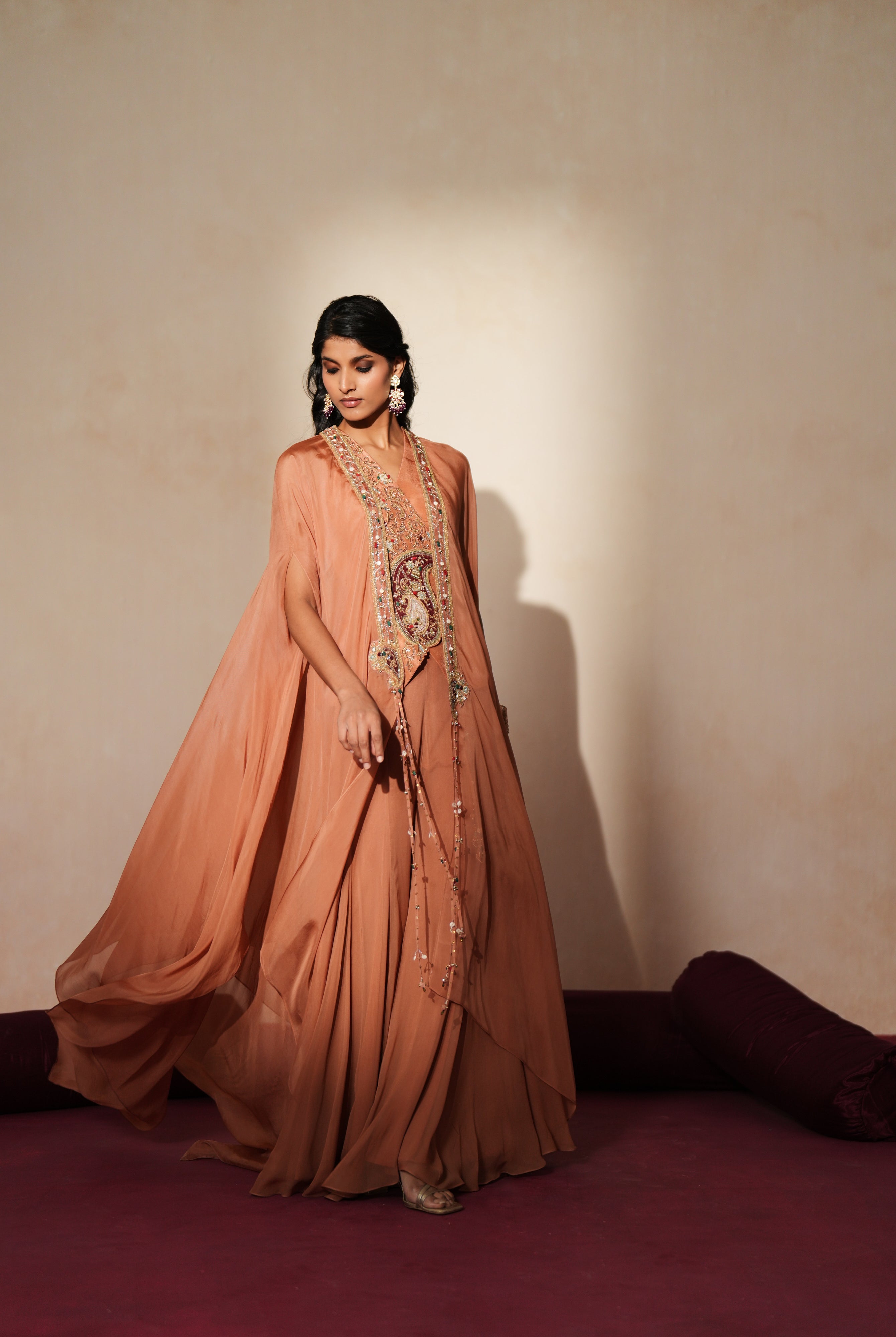 Woman in a metallic mocha traditional outfit standing againsta beige wall on a red carpet.
