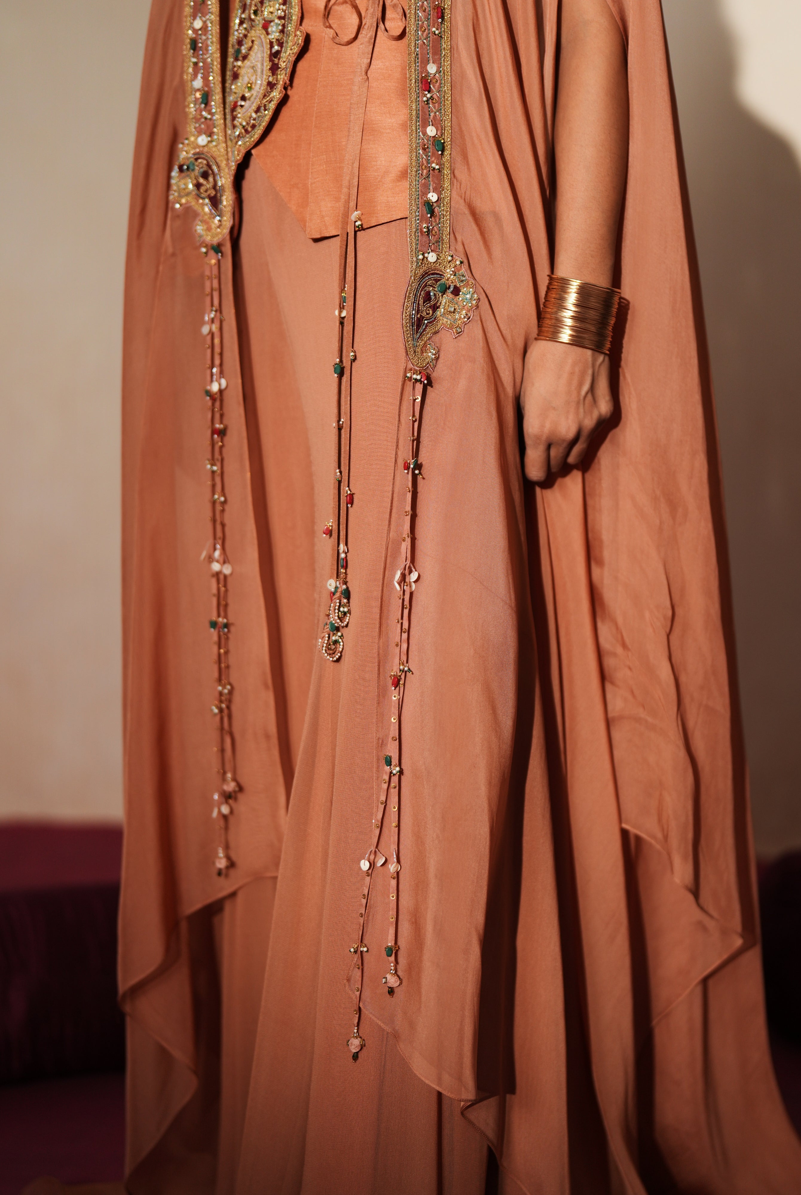 Woman in a metallic mocha traditional outfit standing againsta beige wall on a red carpet.