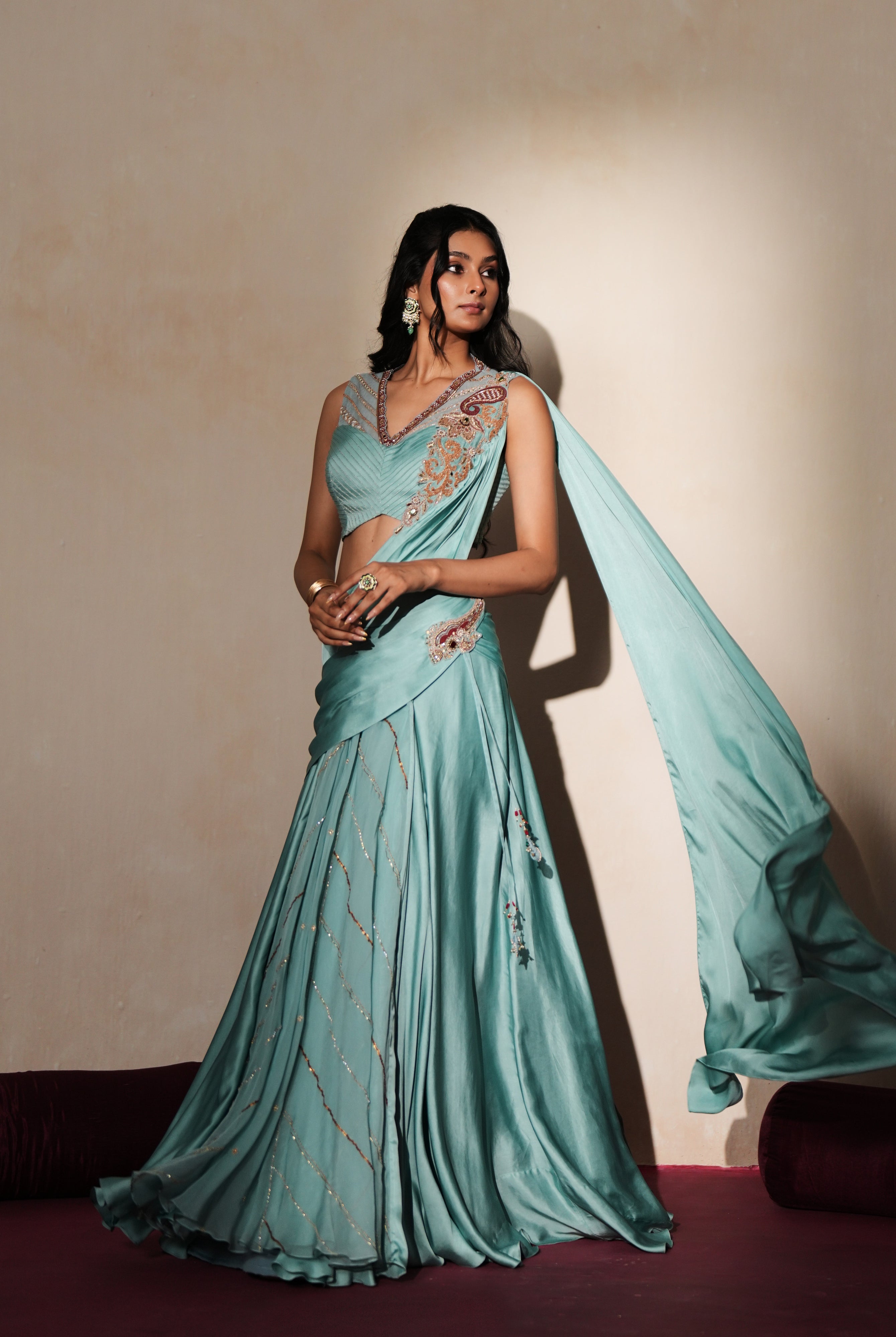 Woman in a pastel blue traditional outfit standing againsta beige wall on a red carpet.