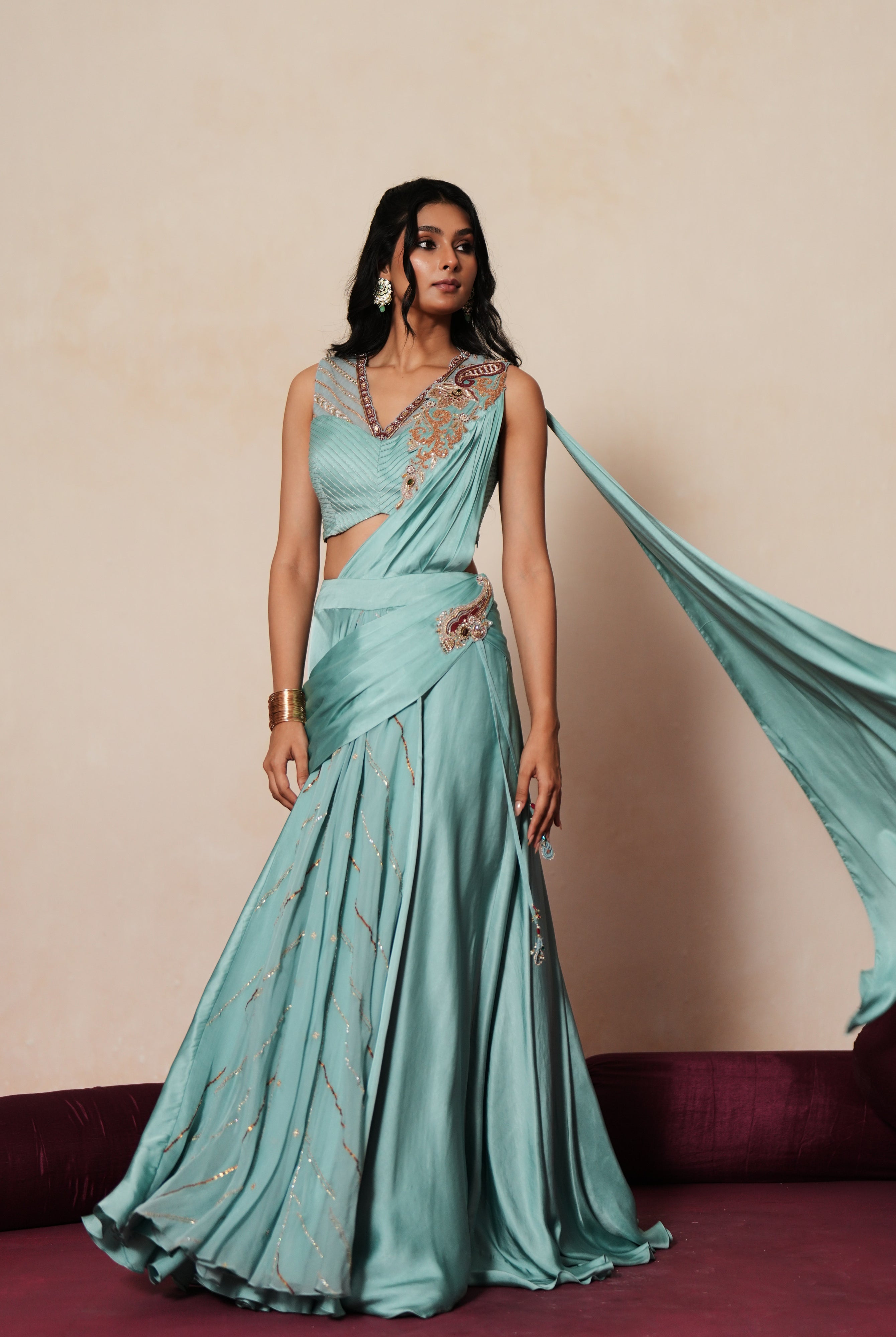 Woman in a pastel blue traditional outfit standing againsta beige wall on a red carpet.