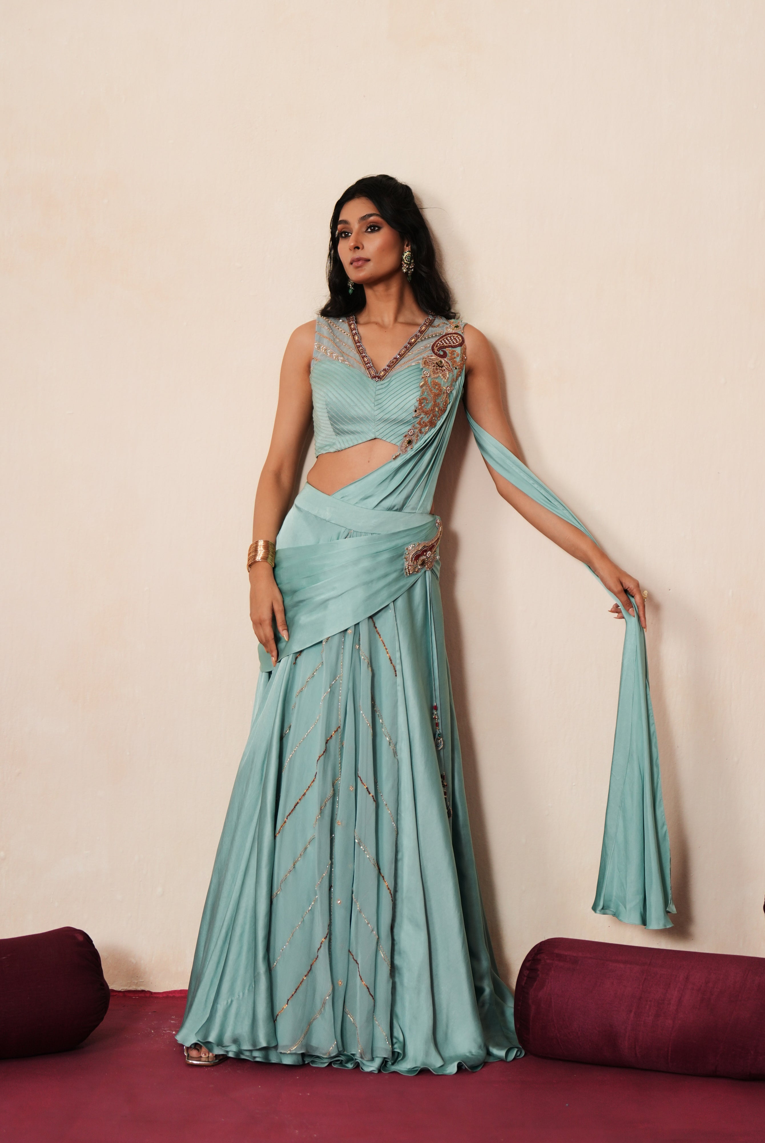 Woman in a pastel blue traditional outfit standing againsta beige wall on a red carpet.