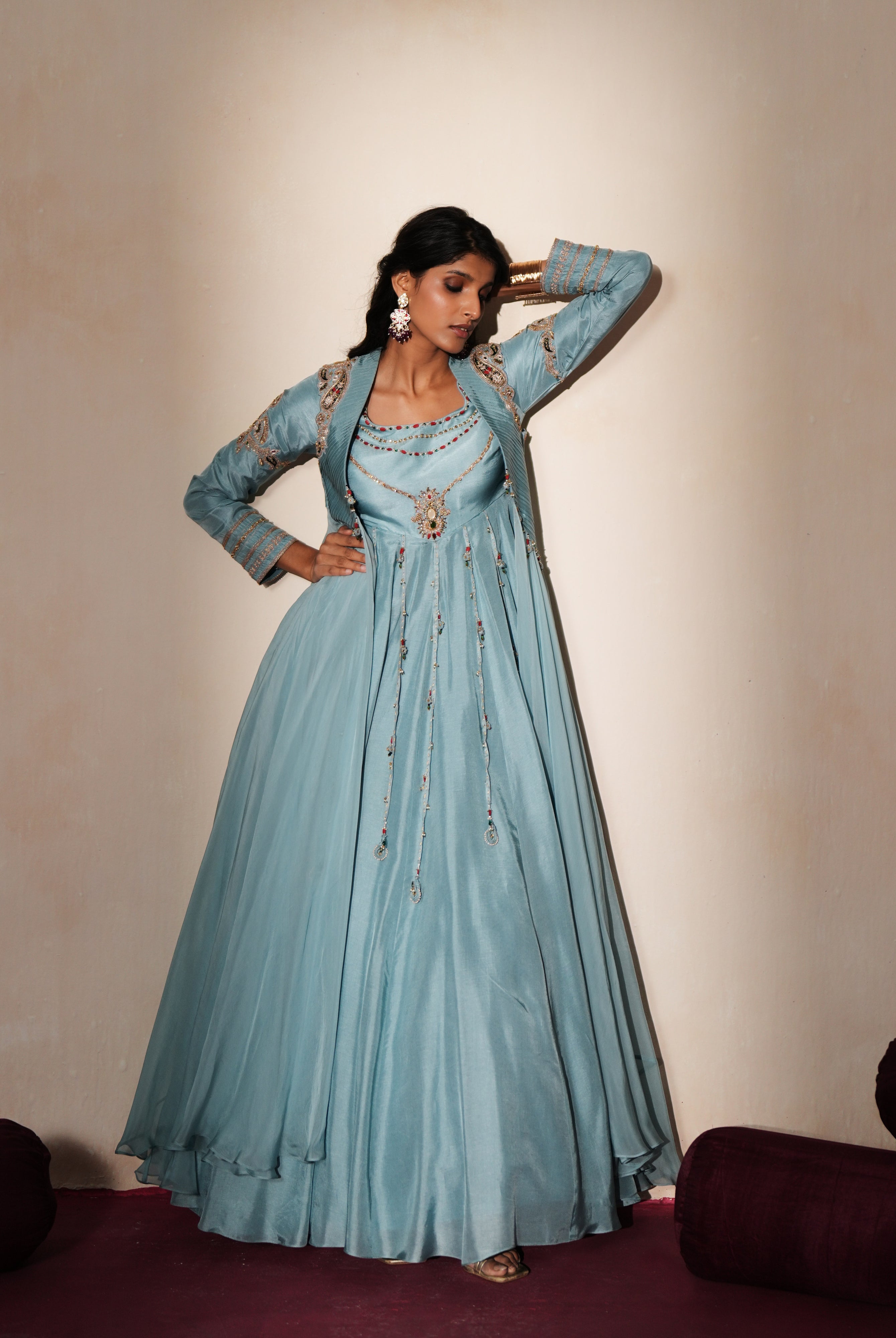 Woman in a pastel blue traditional outfit standing againsta beige wall on a red carpet.