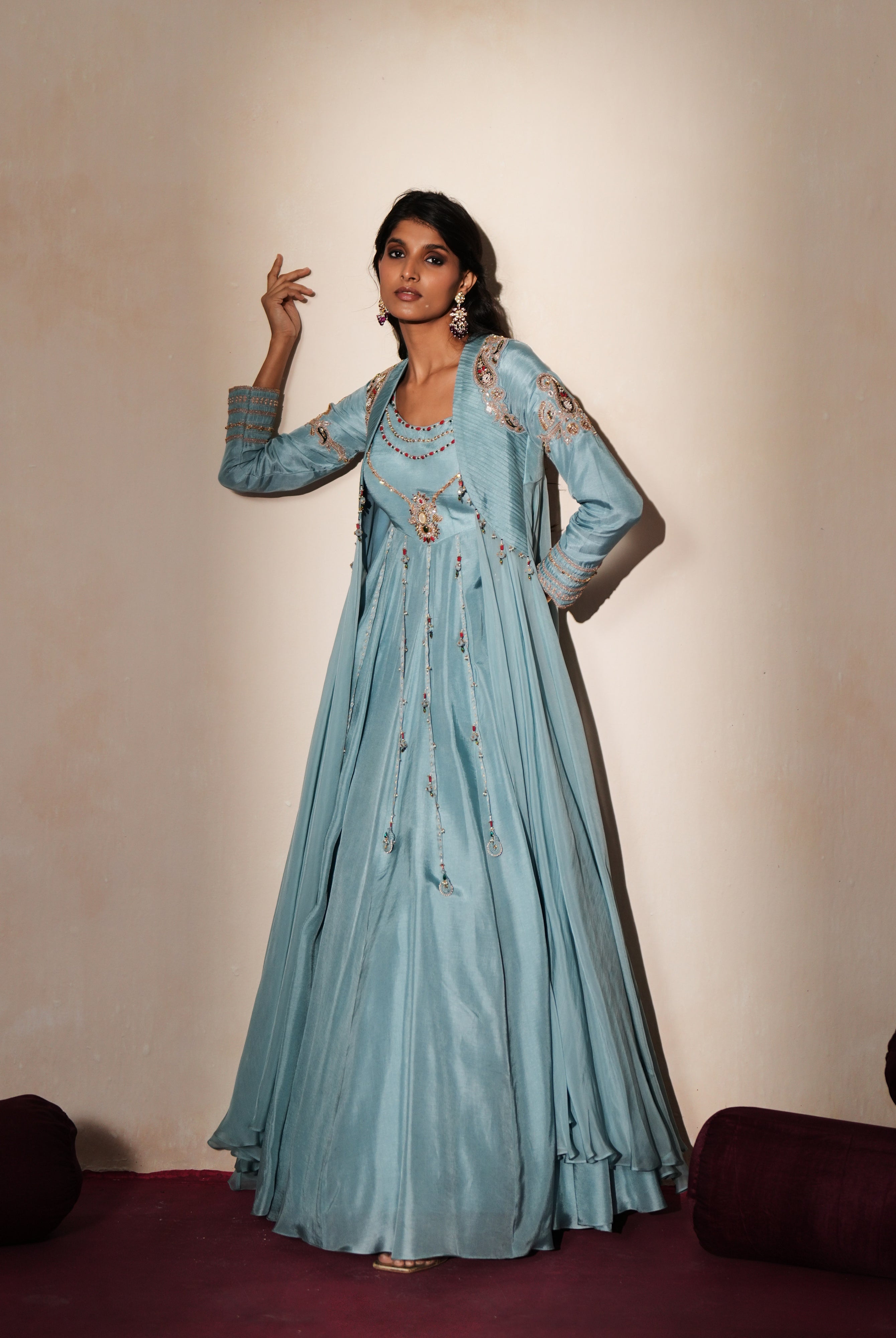 Woman in a pastel blue traditional outfit standing againsta beige wall on a red carpet.