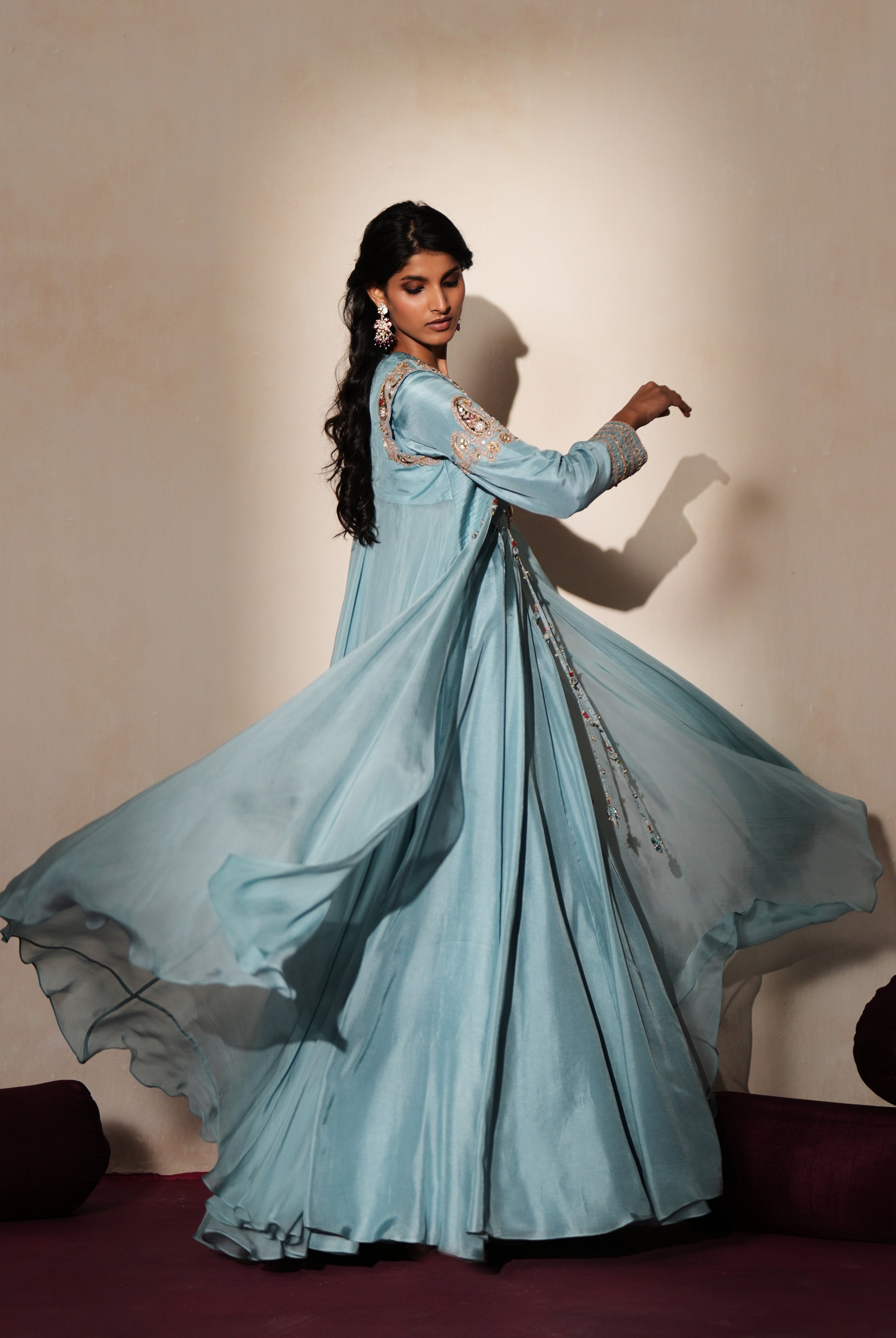 Woman in a pastel blue traditional outfit standing againsta beige wall on a red carpet.