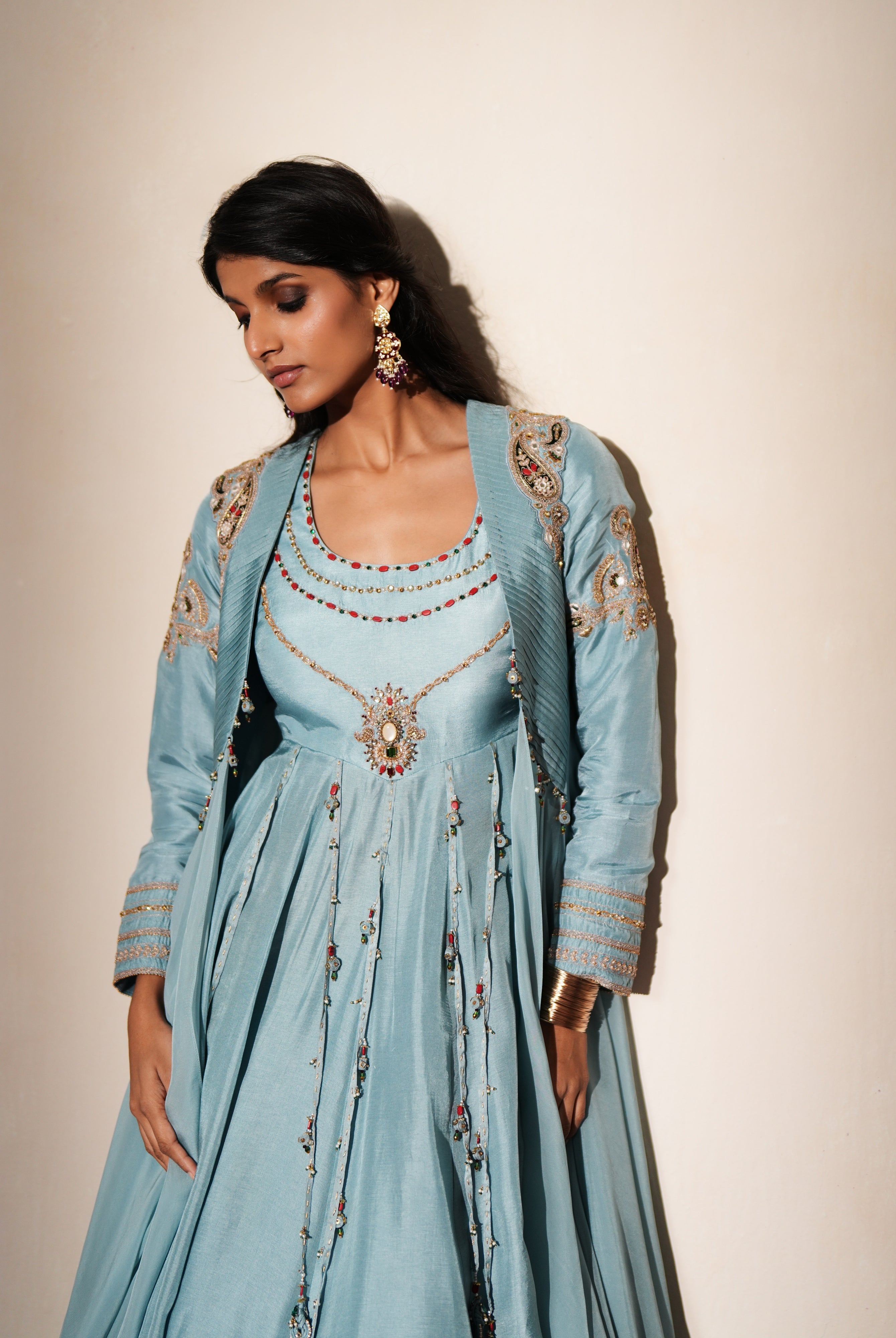 Woman in a pastel blue traditional outfit standing againsta beige wall on a red carpet.