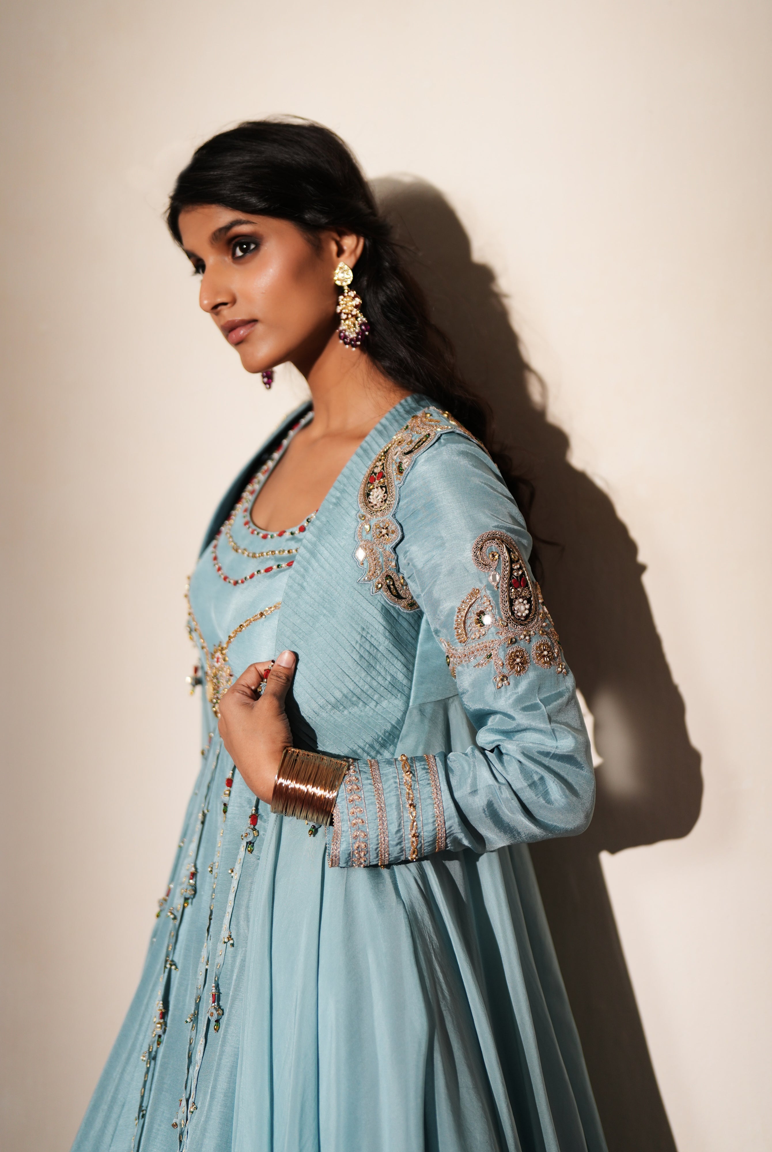 Woman in a pastel blue traditional outfit standing againsta beige wall on a red carpet.