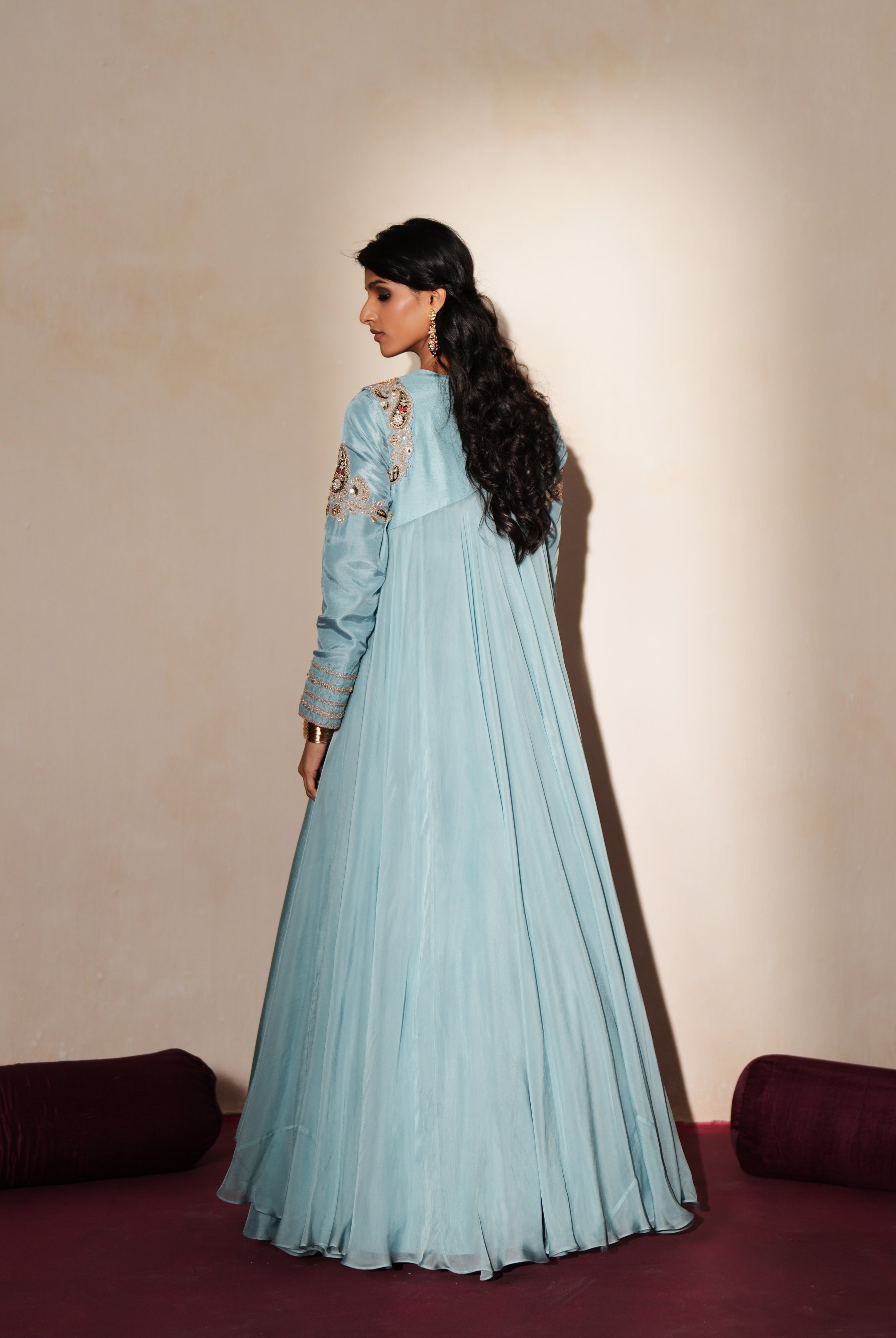 Woman in a pastel blue traditional outfit standing againsta beige wall on a red carpet.