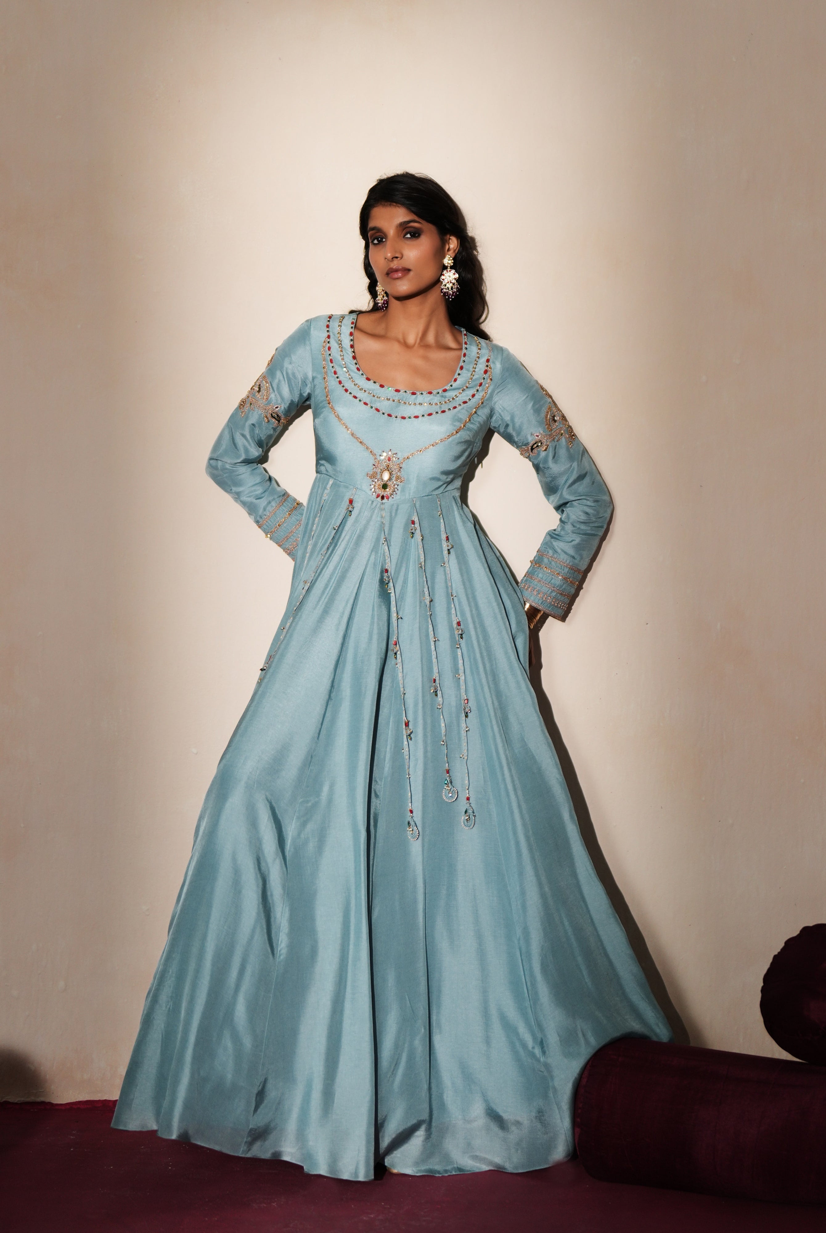 Woman in a pastel blue traditional outfit standing againsta beige wall on a red carpet.