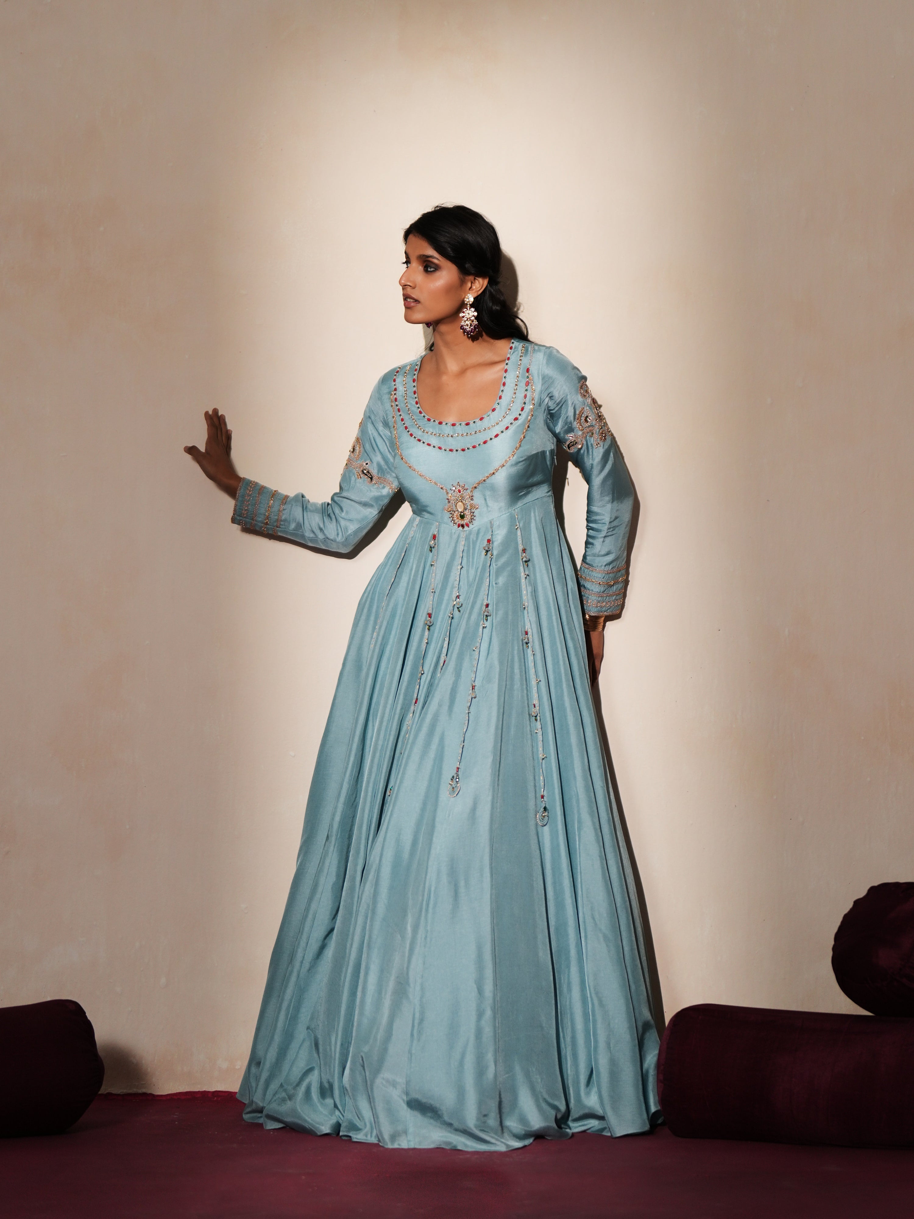 Woman in a pastel blue traditional outfit standing againsta beige wall on a red carpet.