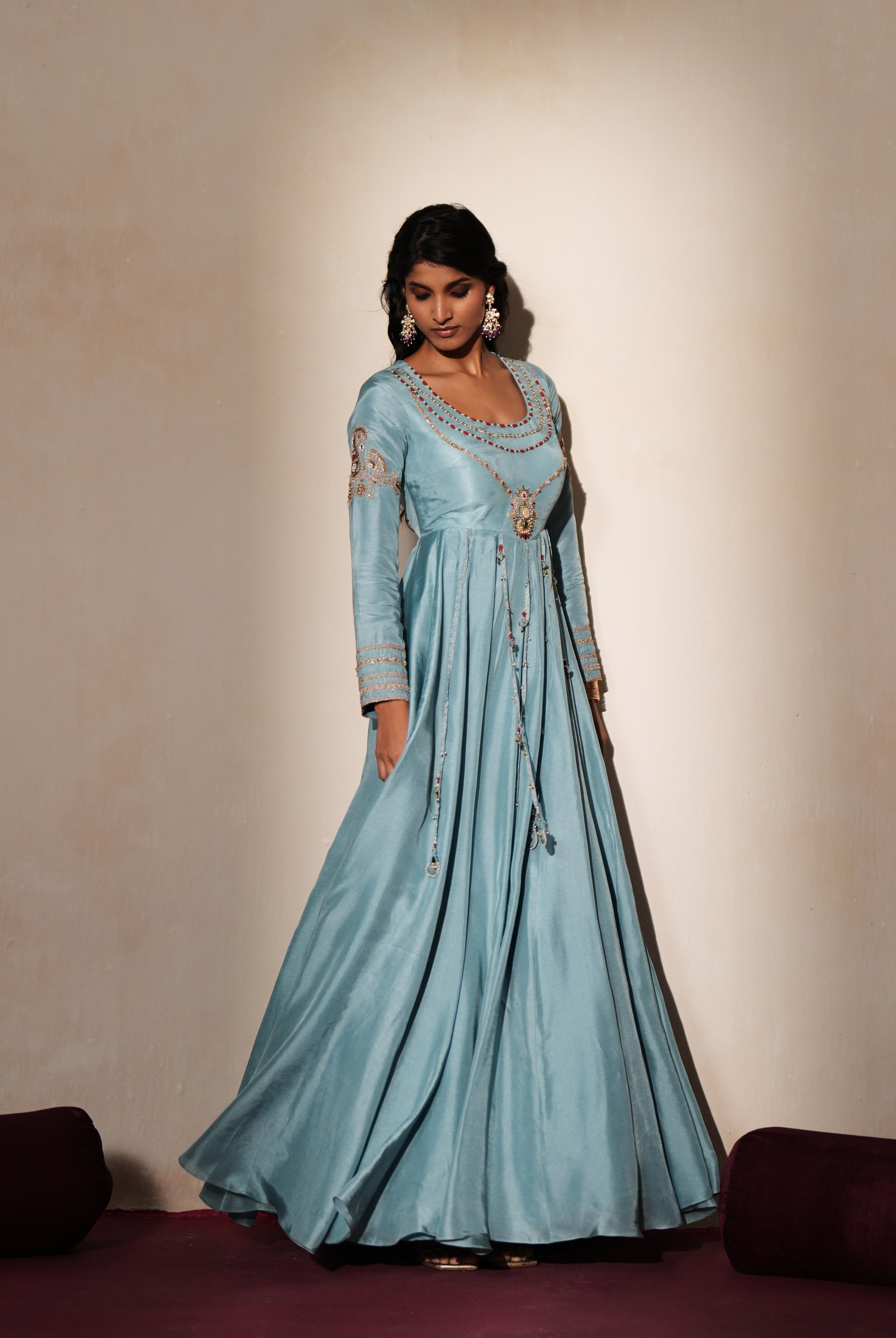 Woman in a pastel blue traditional outfit standing againsta beige wall on a red carpet.