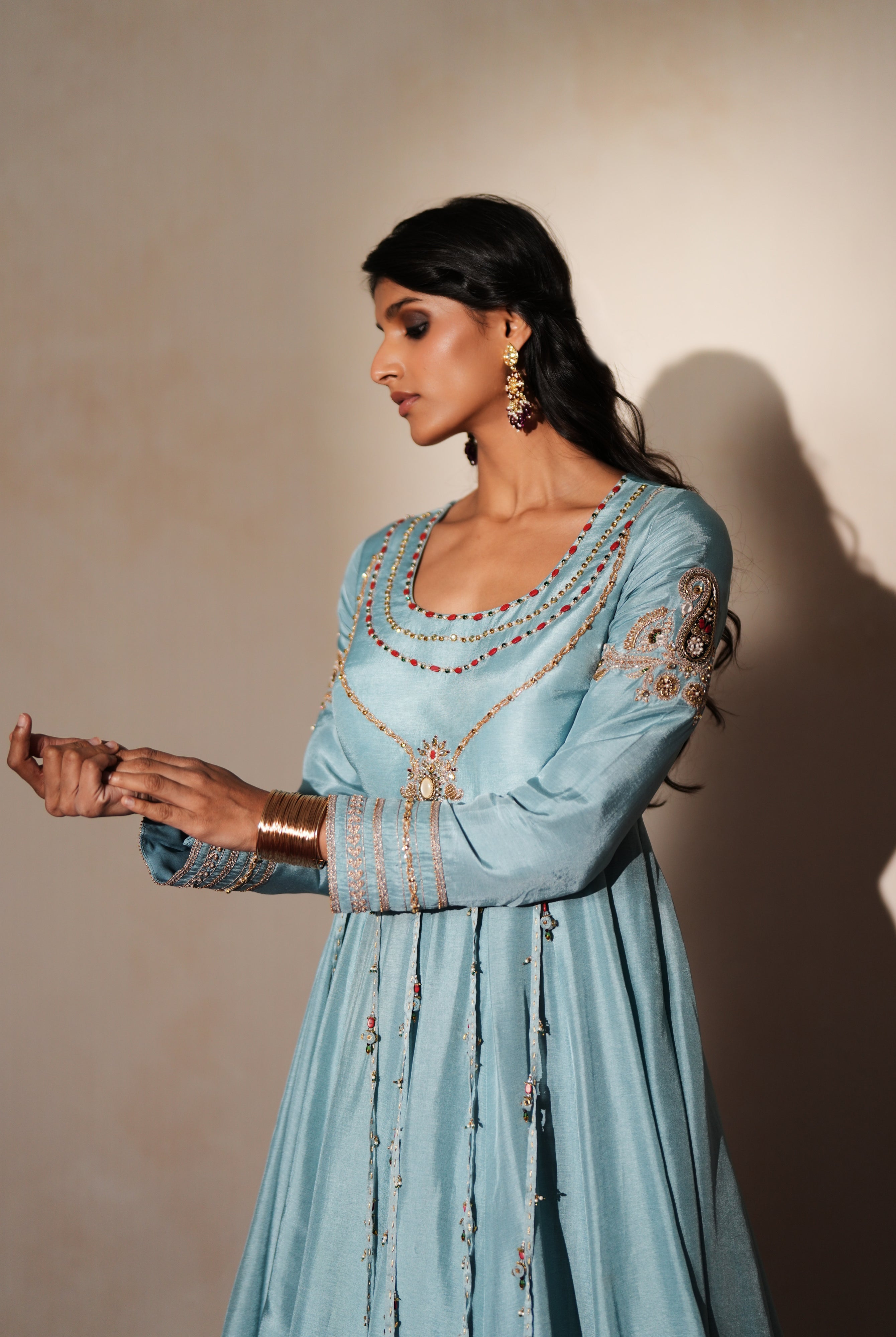 Woman in a pastel blue traditional outfit standing againsta beige wall on a red carpet.
