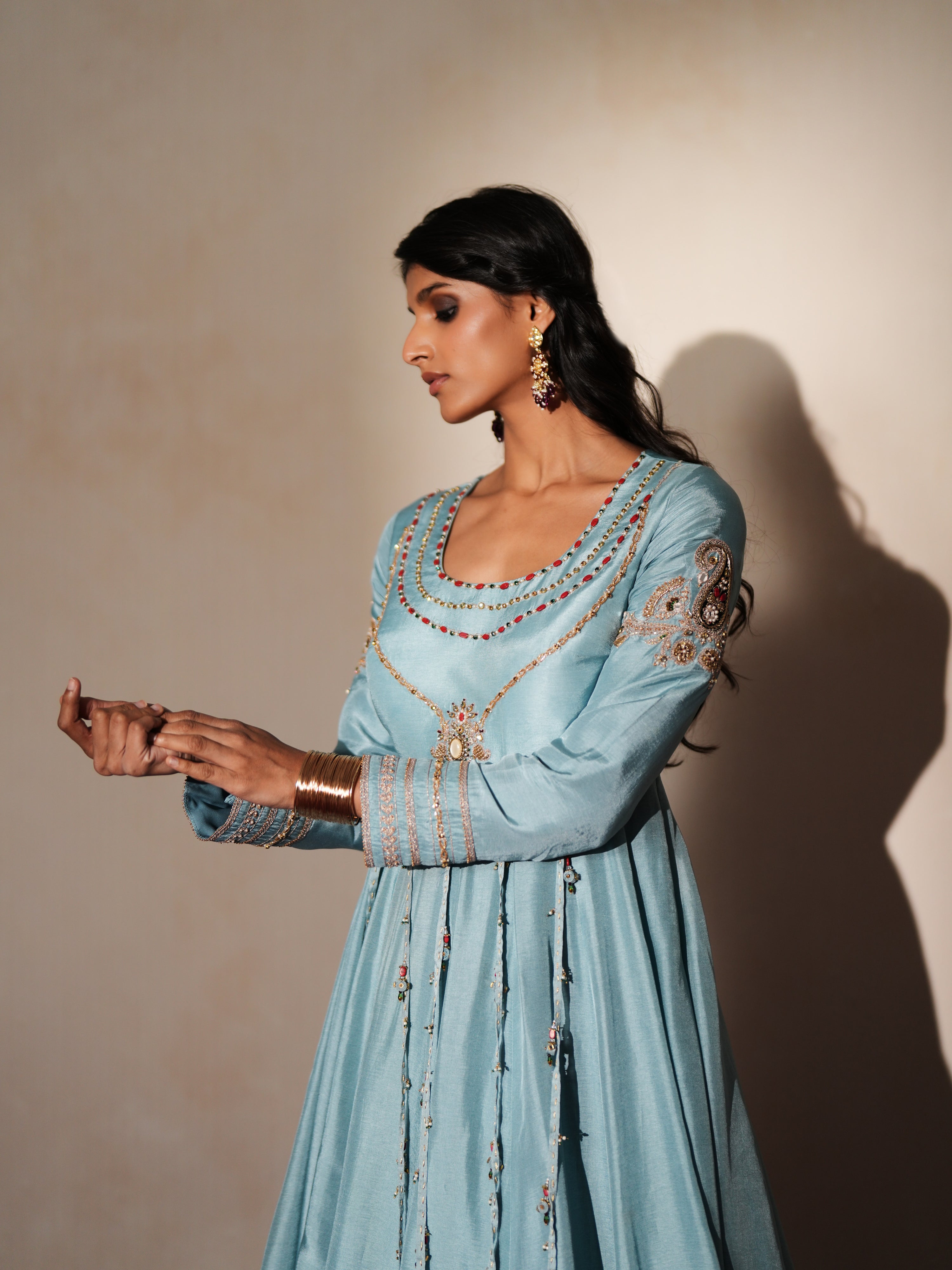 Woman in a pastel blue traditional outfit standing againsta beige wall on a red carpet.