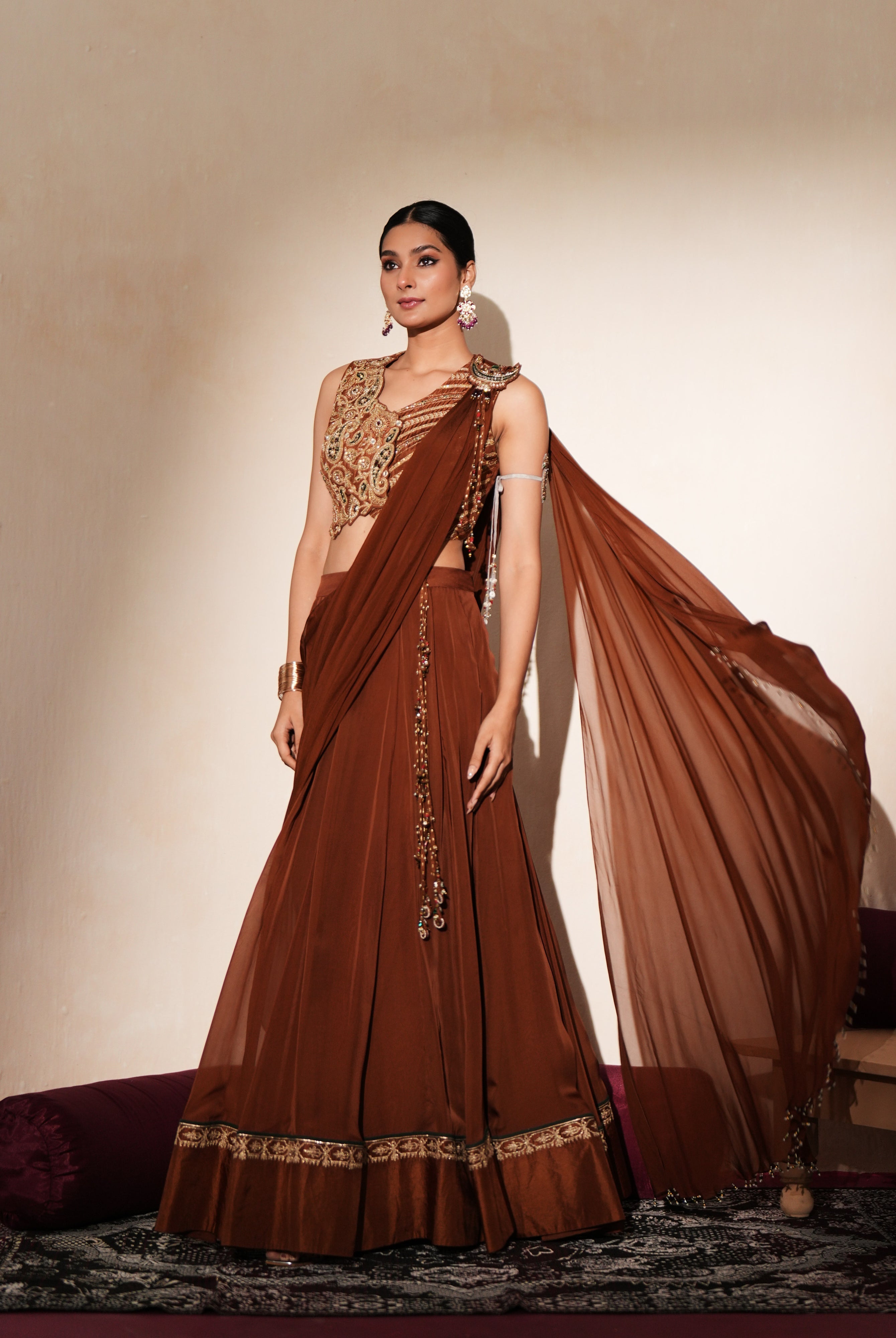 Woman in a mettalic brown traditional outfit standing againsta beige wall on a red carpet.