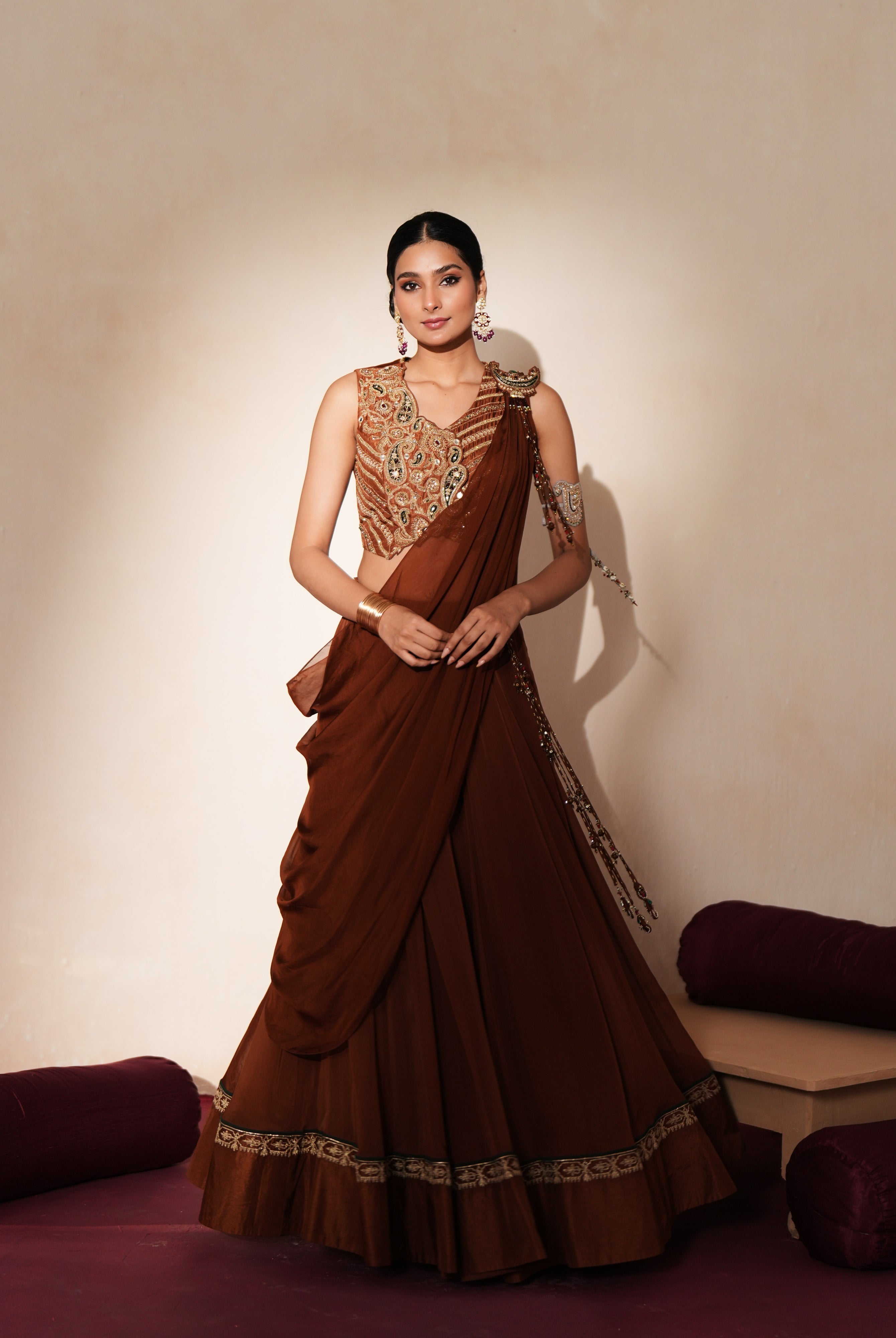 Woman in a mettalic brown traditional outfit standing againsta beige wall on a red carpet.