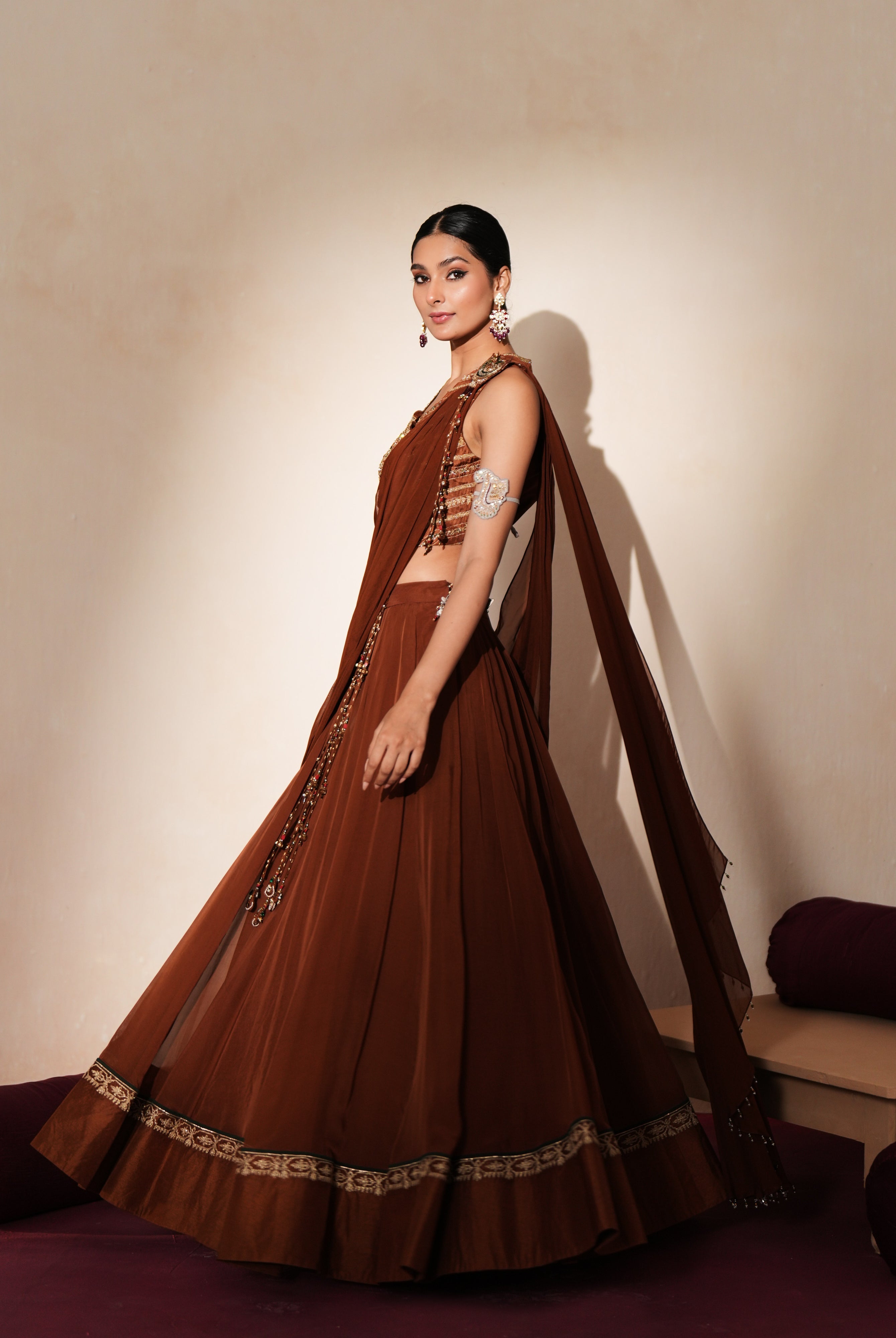 Woman in a mettalic brown traditional outfit standing againsta beige wall on a red carpet.