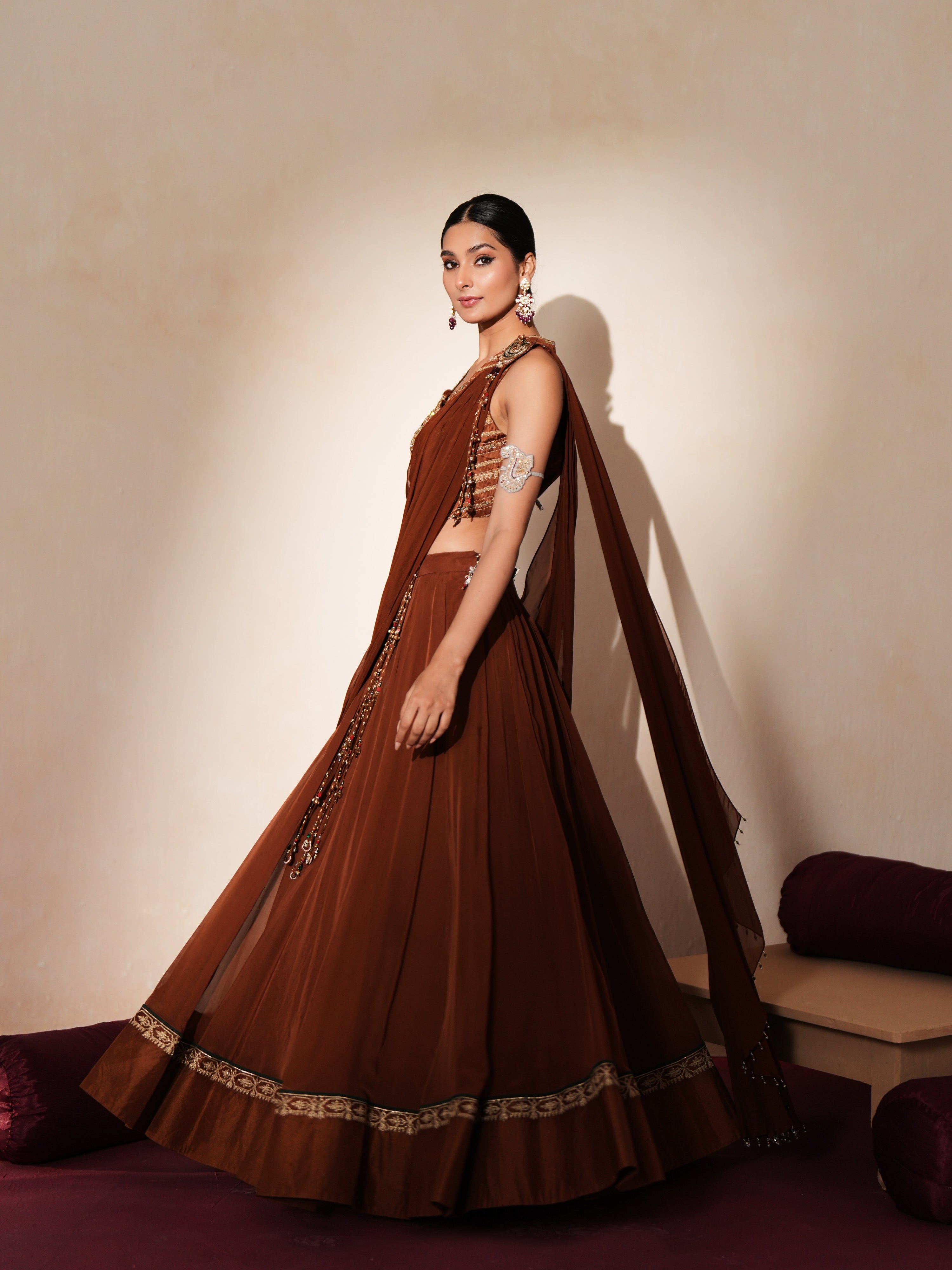 Woman in a mettalic brown traditional outfit standing againsta beige wall on a red carpet.