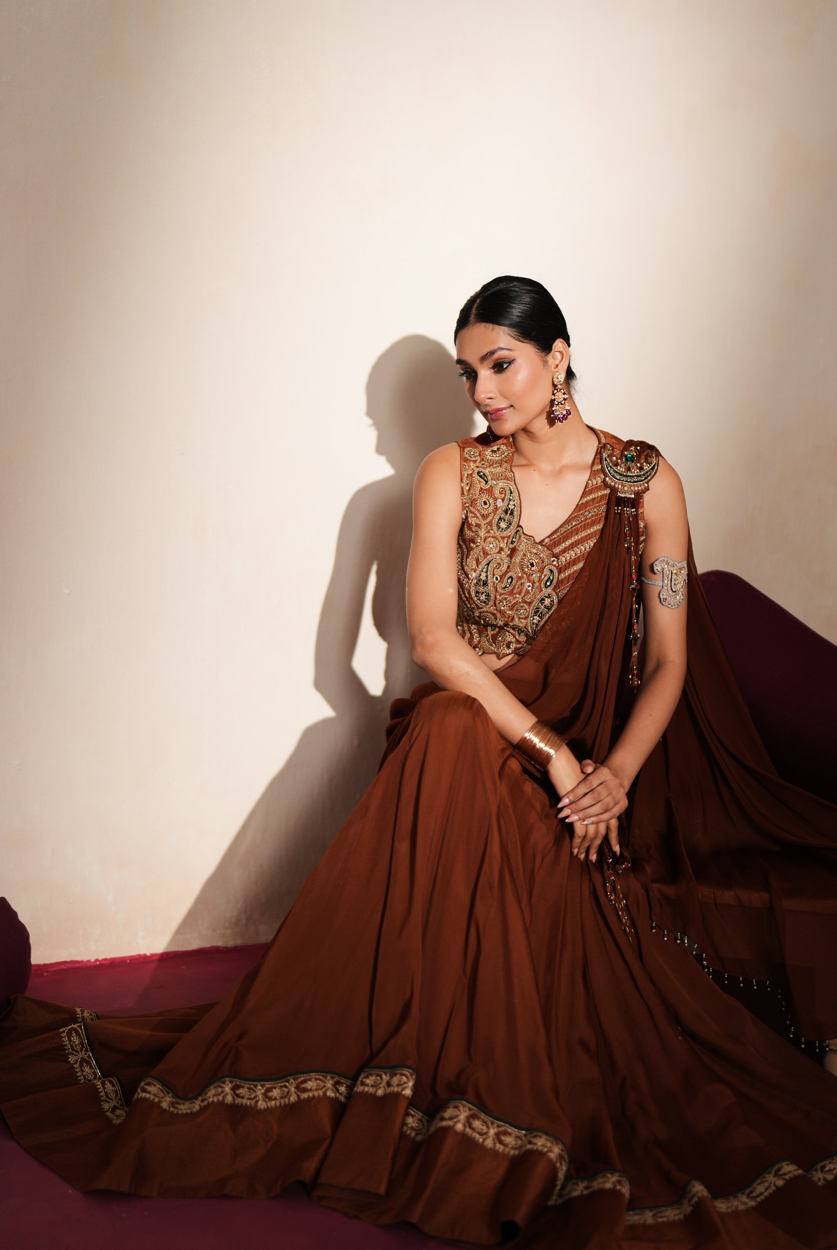 Woman in a mettalic brown traditional outfit standing againsta beige wall on a red carpet.