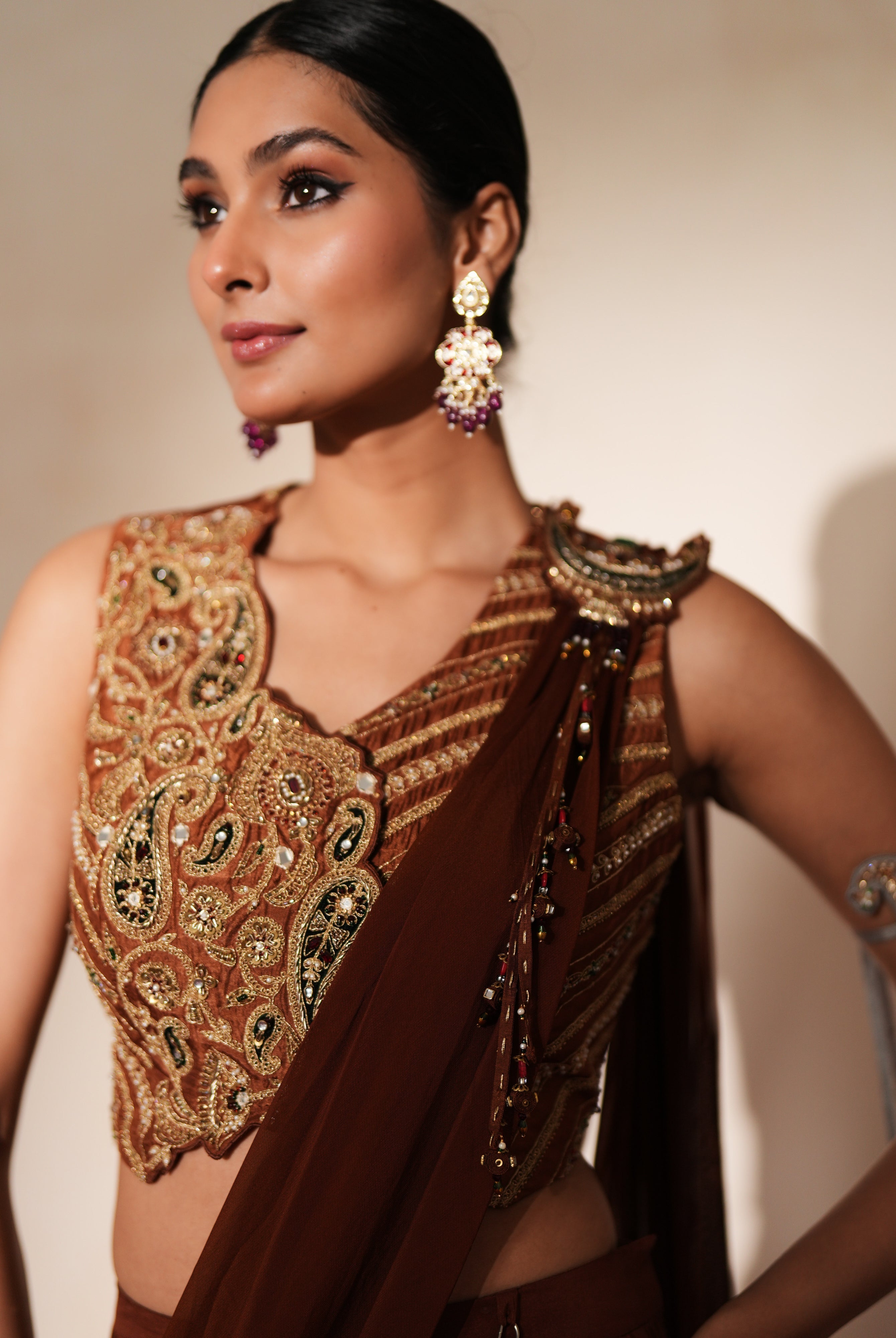 Woman in a mettalic brown traditional outfit standing againsta beige wall on a red carpet.