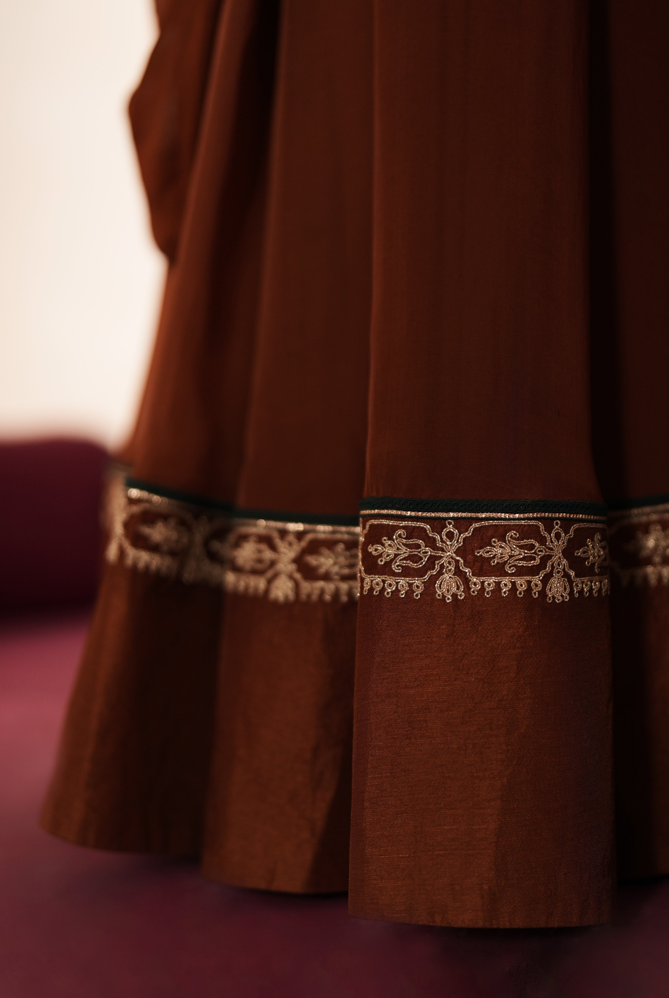 Woman in a mettalic brown traditional outfit standing againsta beige wall on a red carpet.